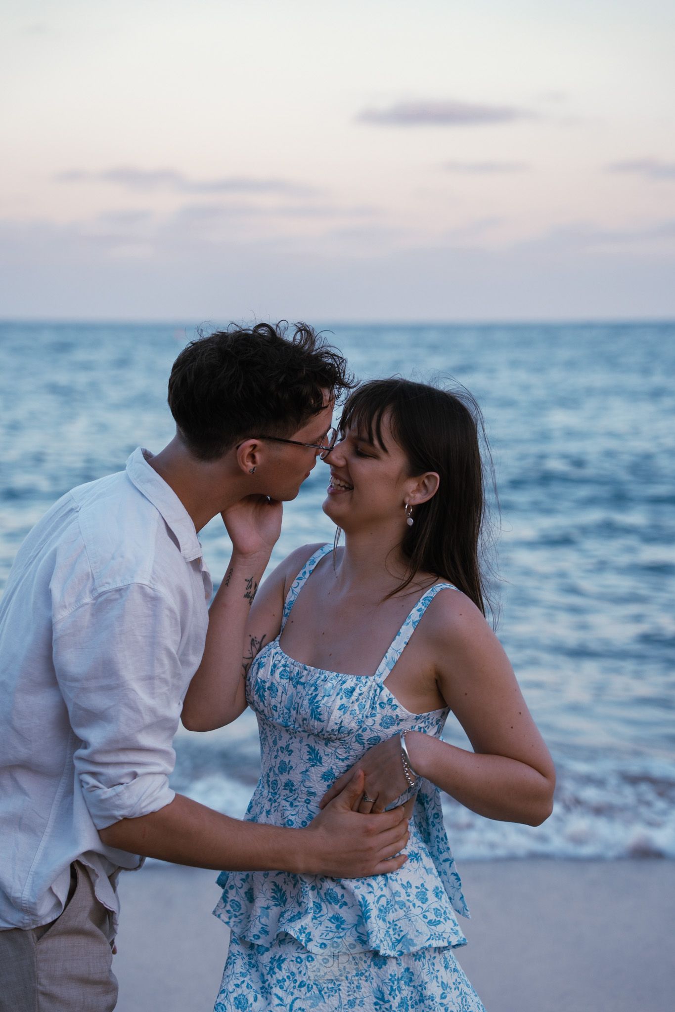 A romantic couple shares an intimate moment at sunset on a beach with the ocean in the background.