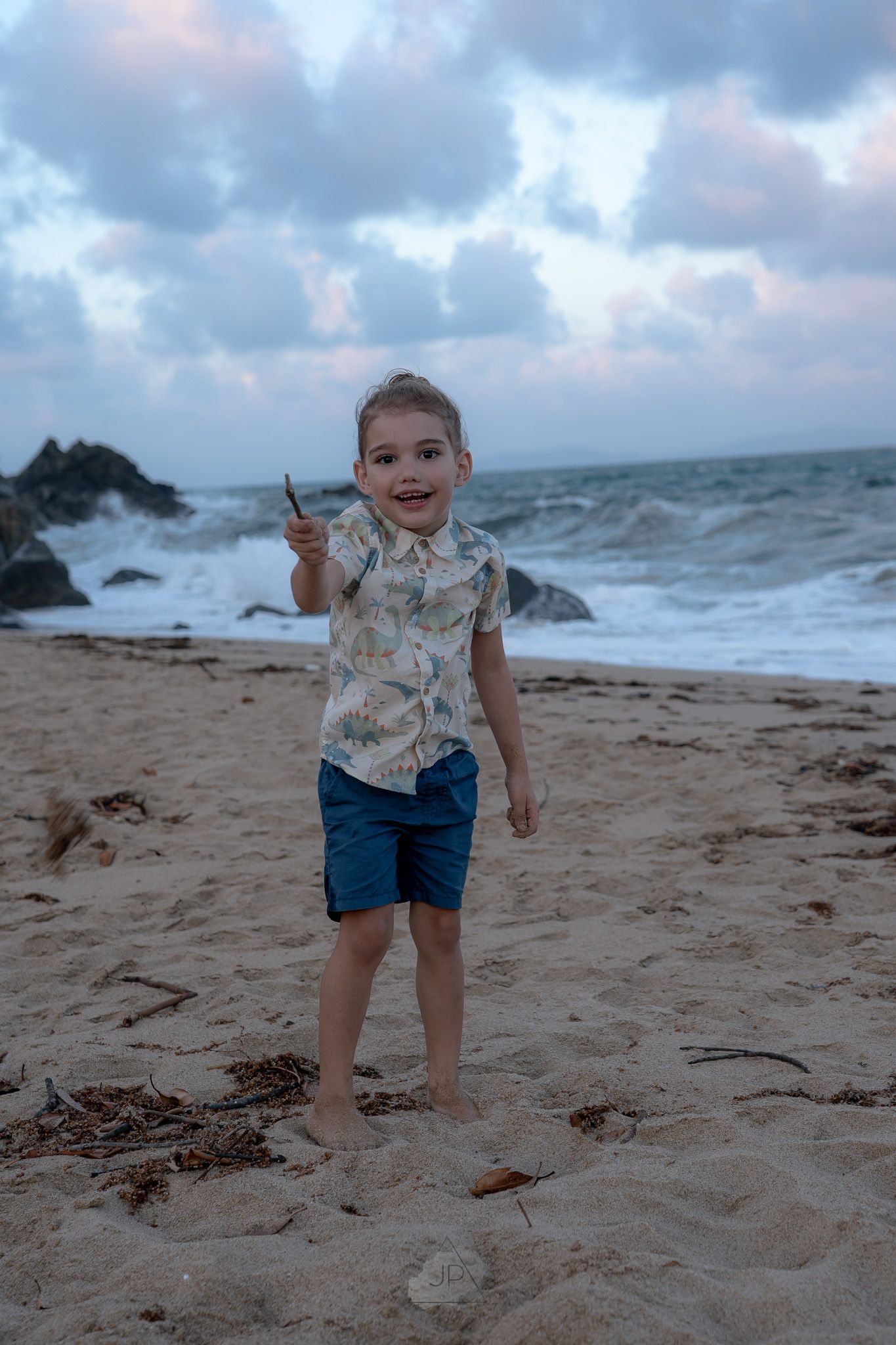 Child playing in the sand on a moody beach with dramatic clouds and ocean waves in the background.
