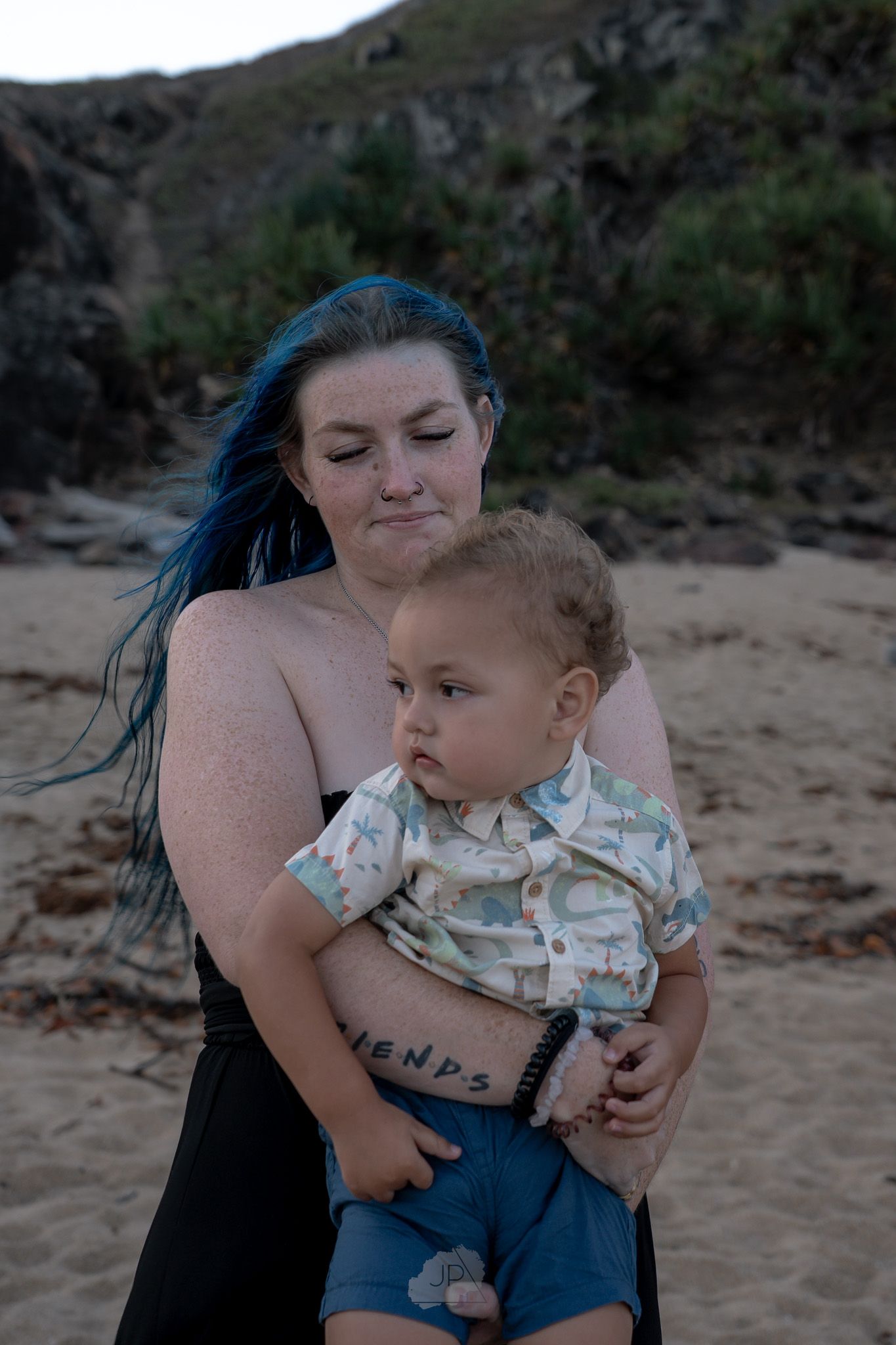 A tender moment shared between parent and child playing together on a sandy beach with rocky cliffs in the background.