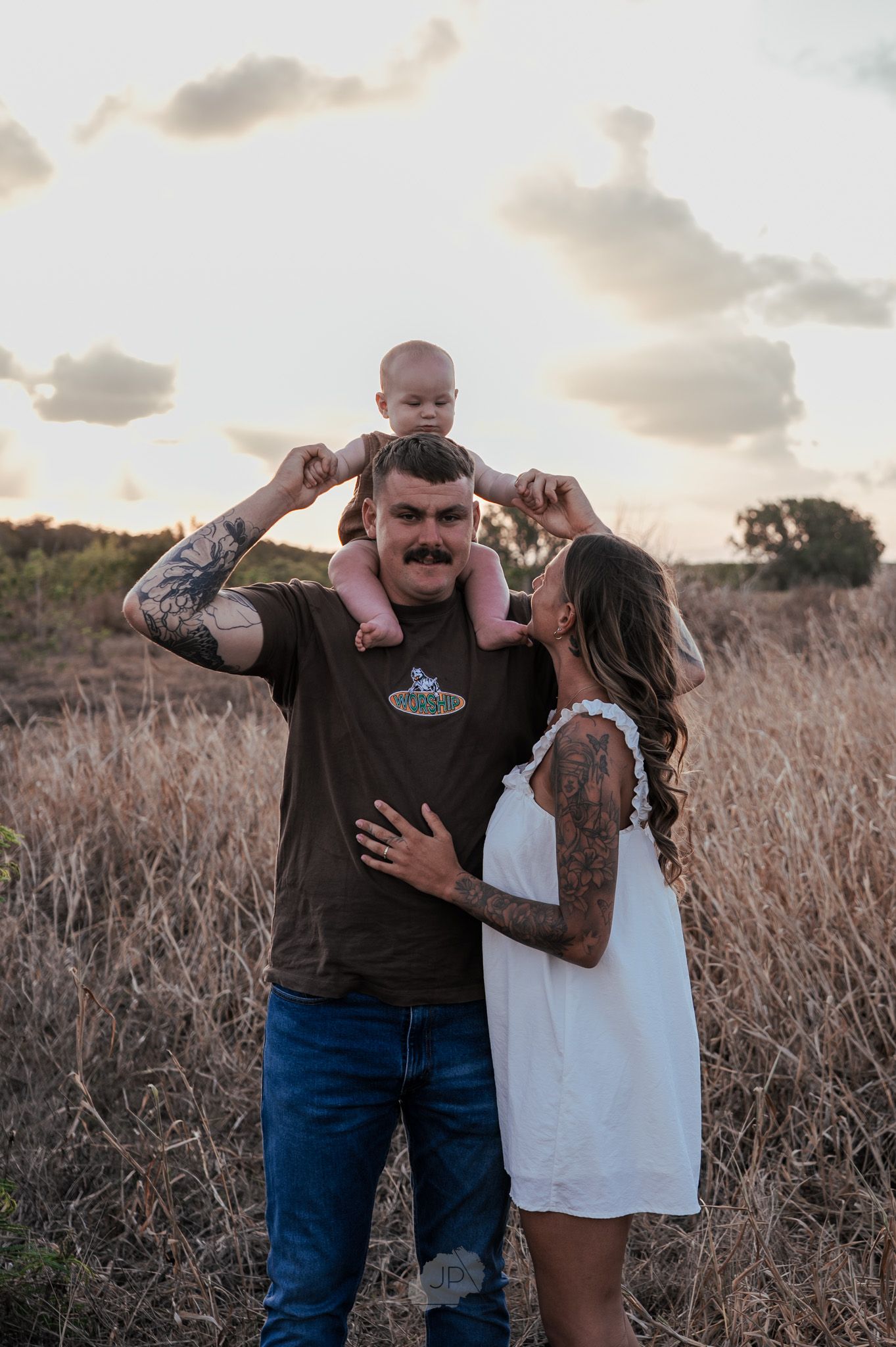 A couple shares a romantic moment in a field of tall grass during sunset.