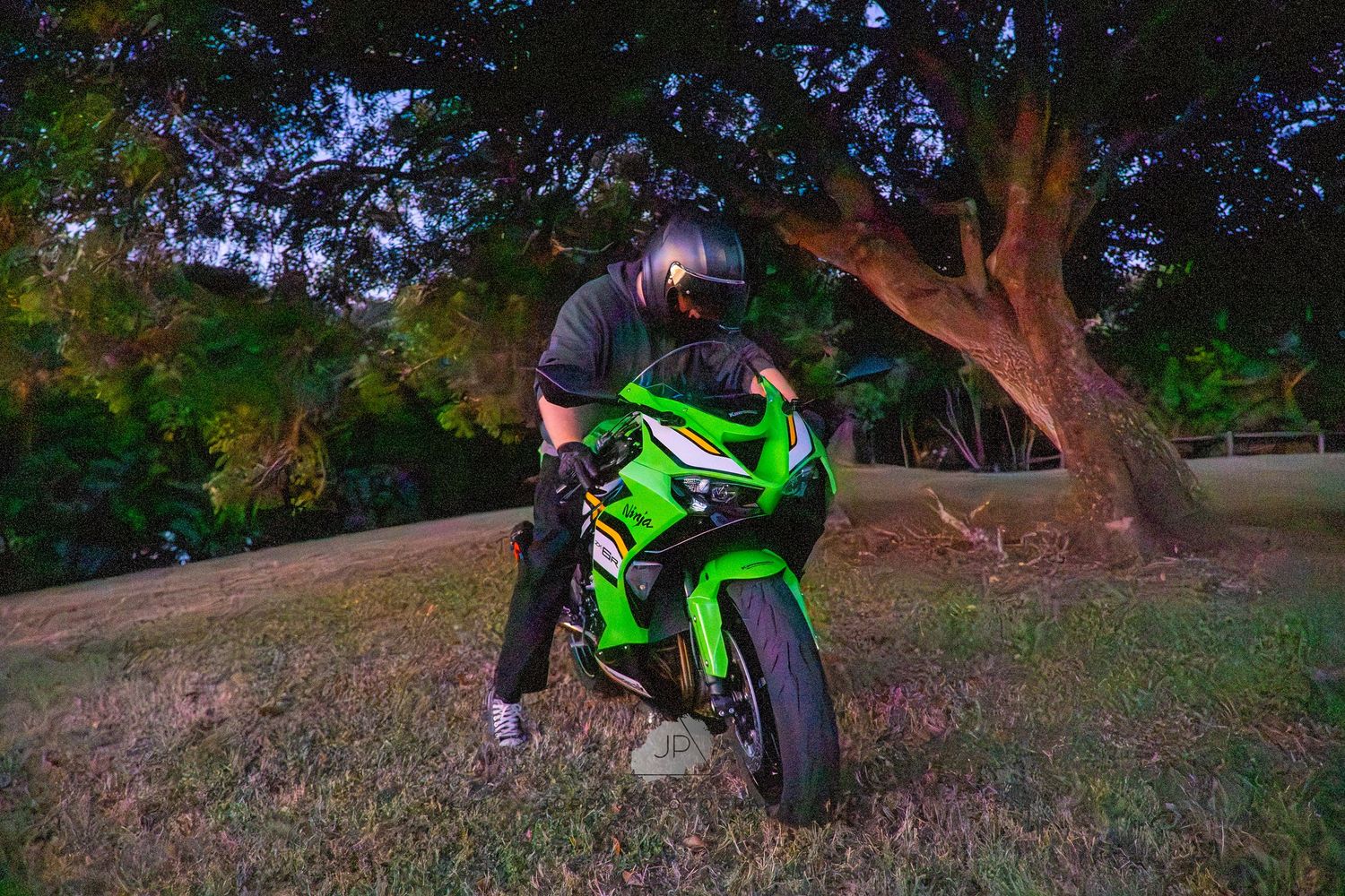 A person performs tricks on a bright green ATV while riding through a grassy outdoor area in the daylight.