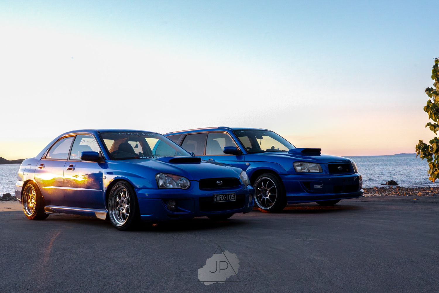 A row of blue BMW M3 cars parked at sunset with orange sky in the background.