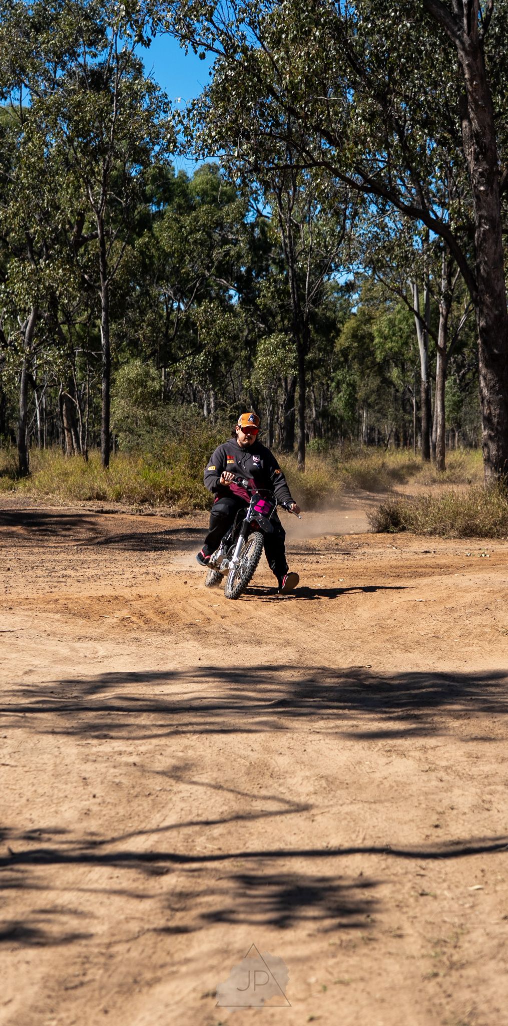 A dirt bike rider performs a sliding turn maneuver on a dusty trail through eucalyptus trees in Australia.