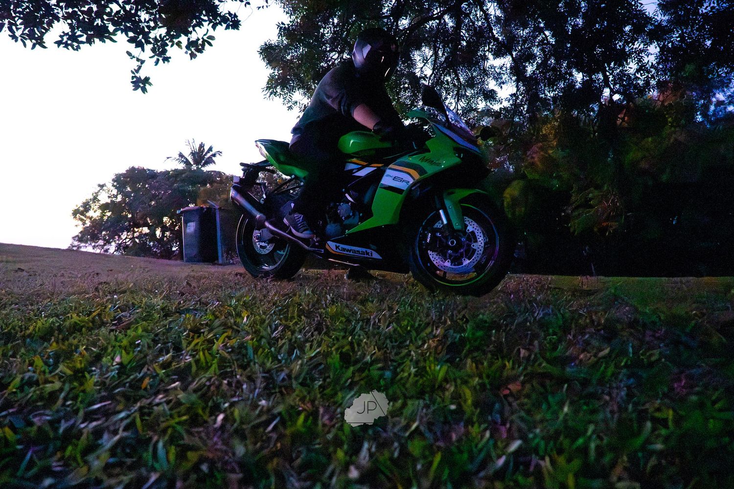 A bright green sport motorcycle sits at rest on a grassy hill during sunset.