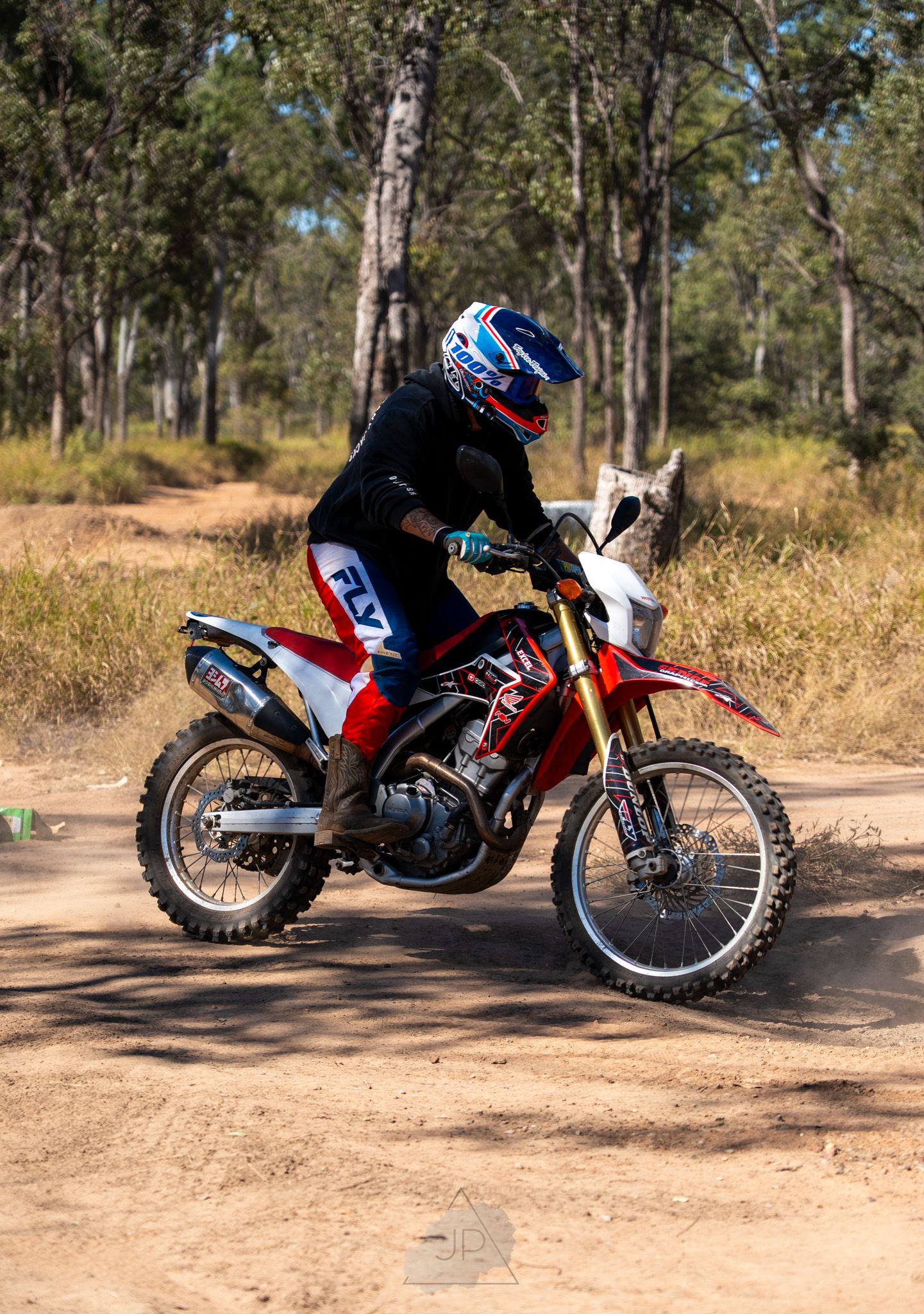 A red Honda XR400 dirt bike parked on a dirt trail surrounded by eucalyptus trees in an off-road setting.