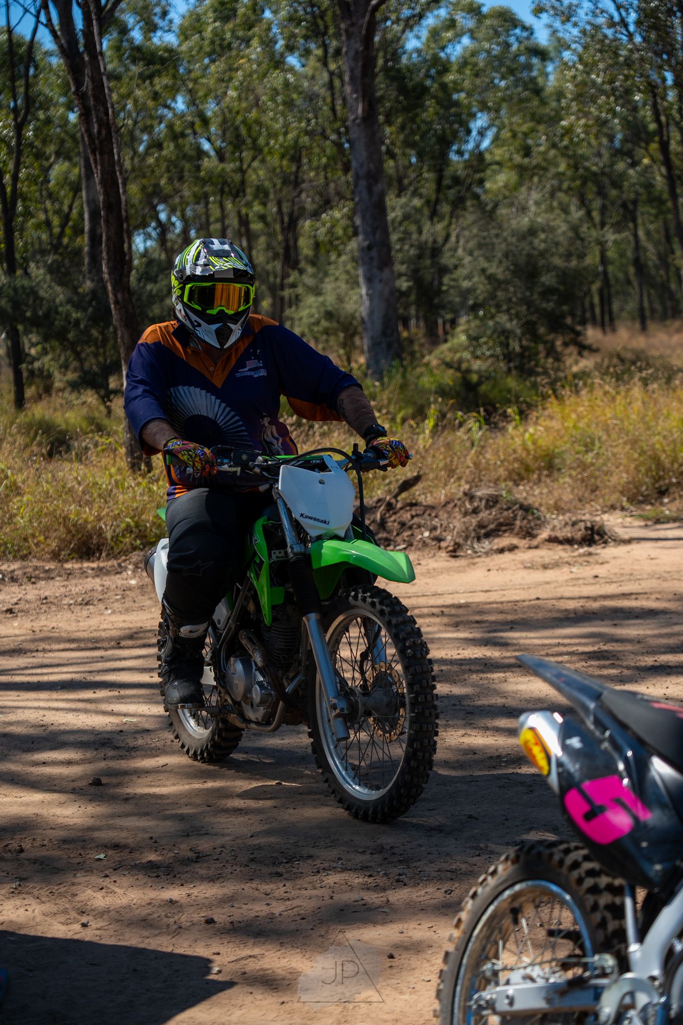 Off-road motorcycle rider navigating a dirt trail through eucalyptus forest on a sunny day.