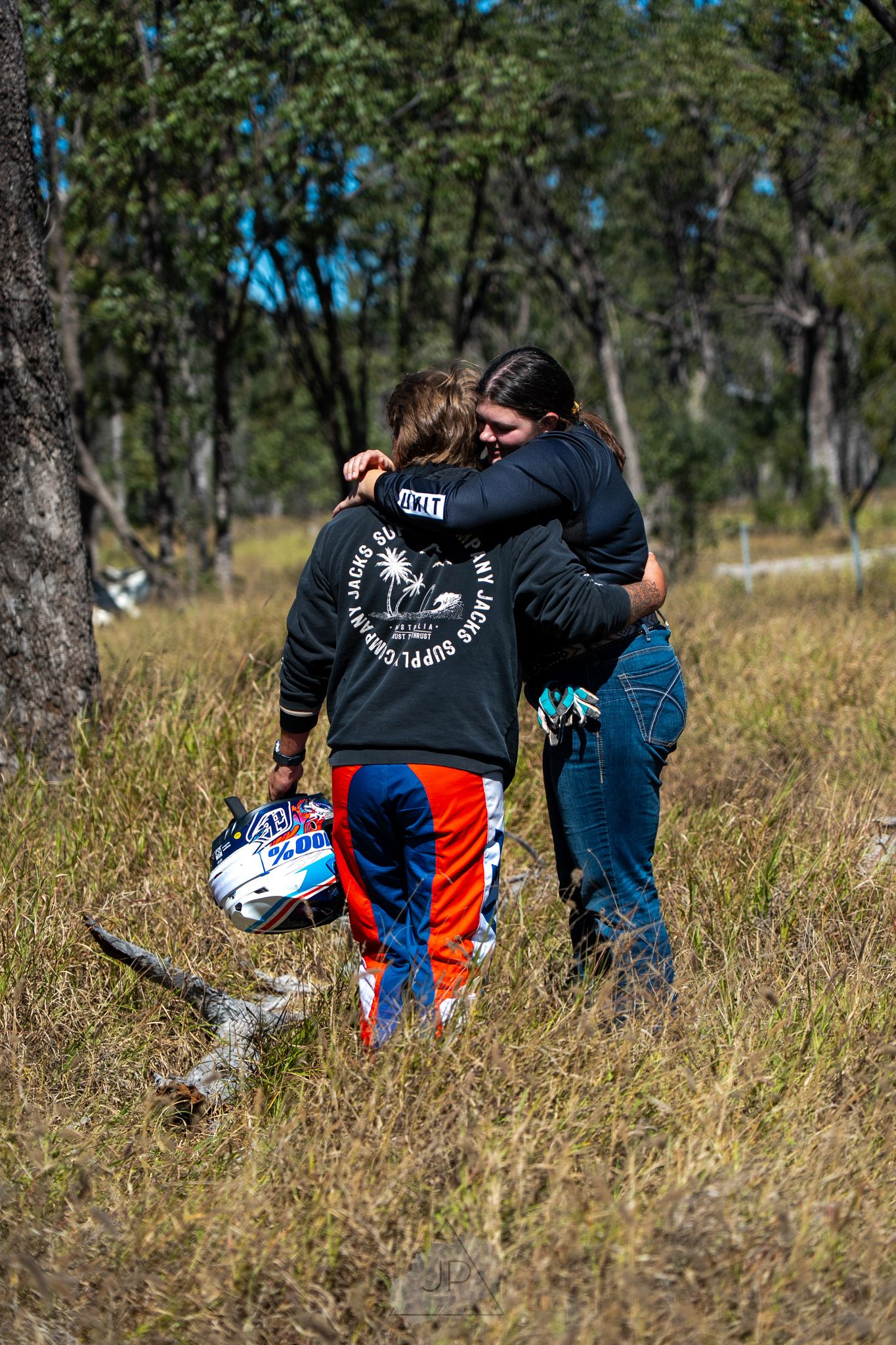 Two people sitting in tall grass under trees sharing an intimate moment.