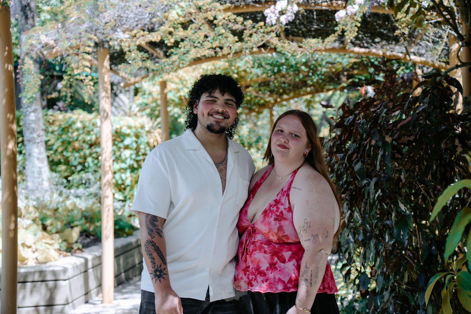 A couple stands close together in a garden setting with trees and foliage in the background.