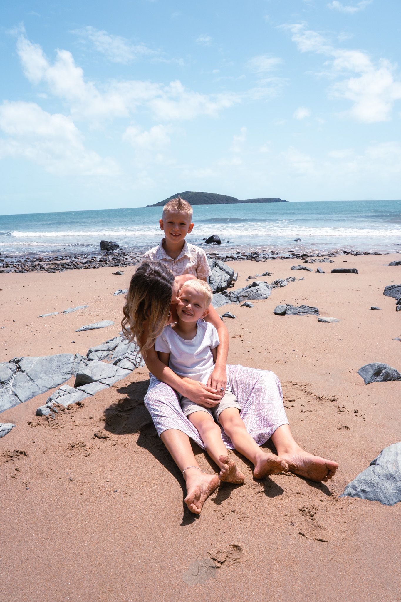 A family relaxes together on a scenic beach with rocky outcrops and blue ocean waters on a sunny summer day.