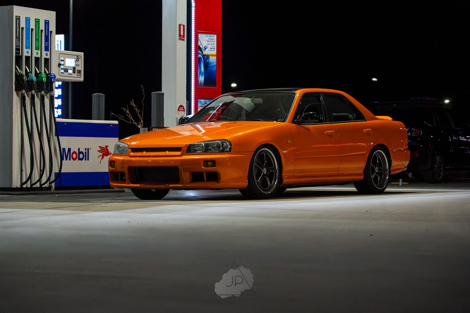 A bright orange sports car parked at a gas station at night with dramatic lighting.