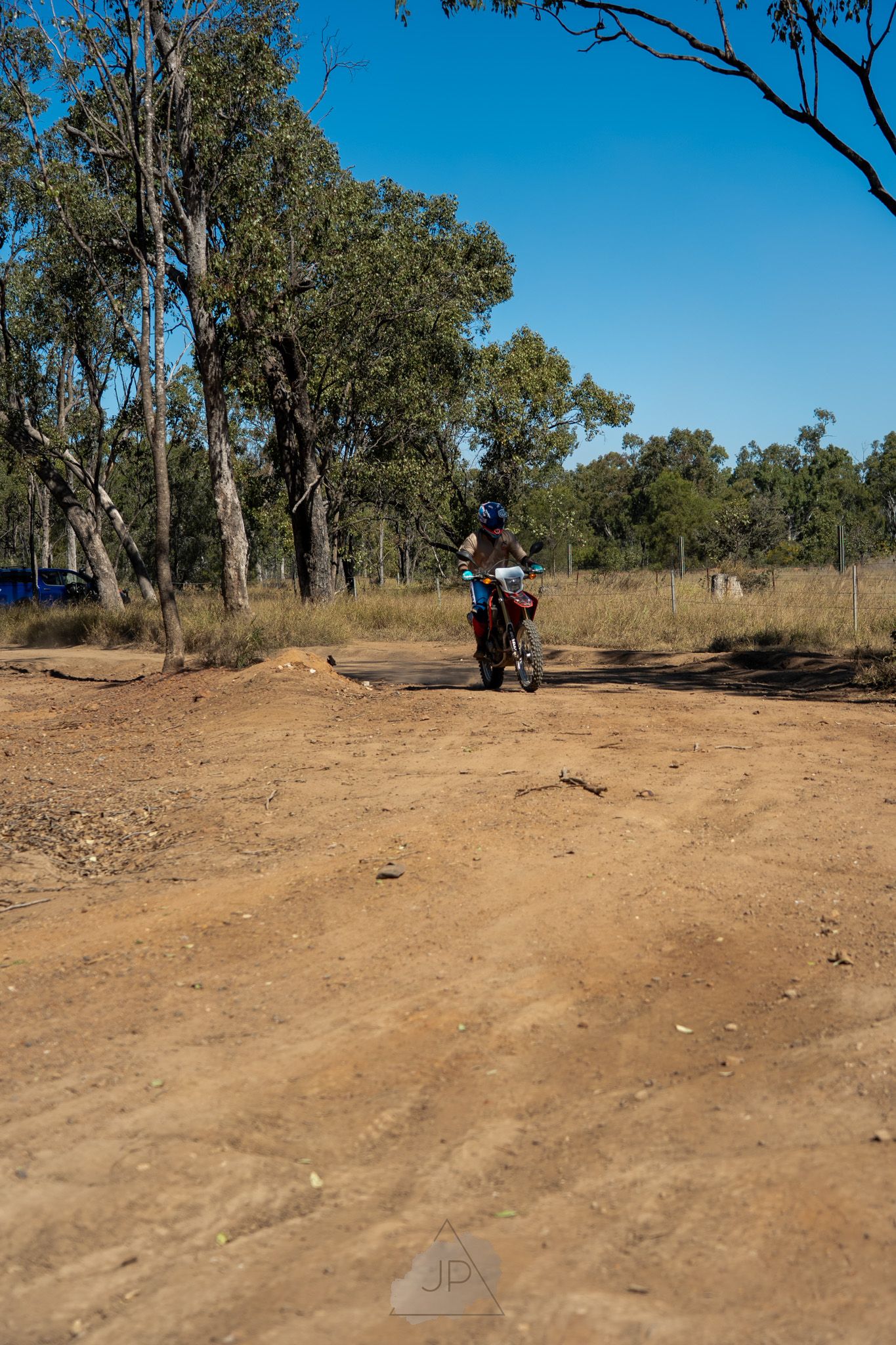 A dirt trail winds through a wooded area with eucalyptus trees under a bright blue sky.