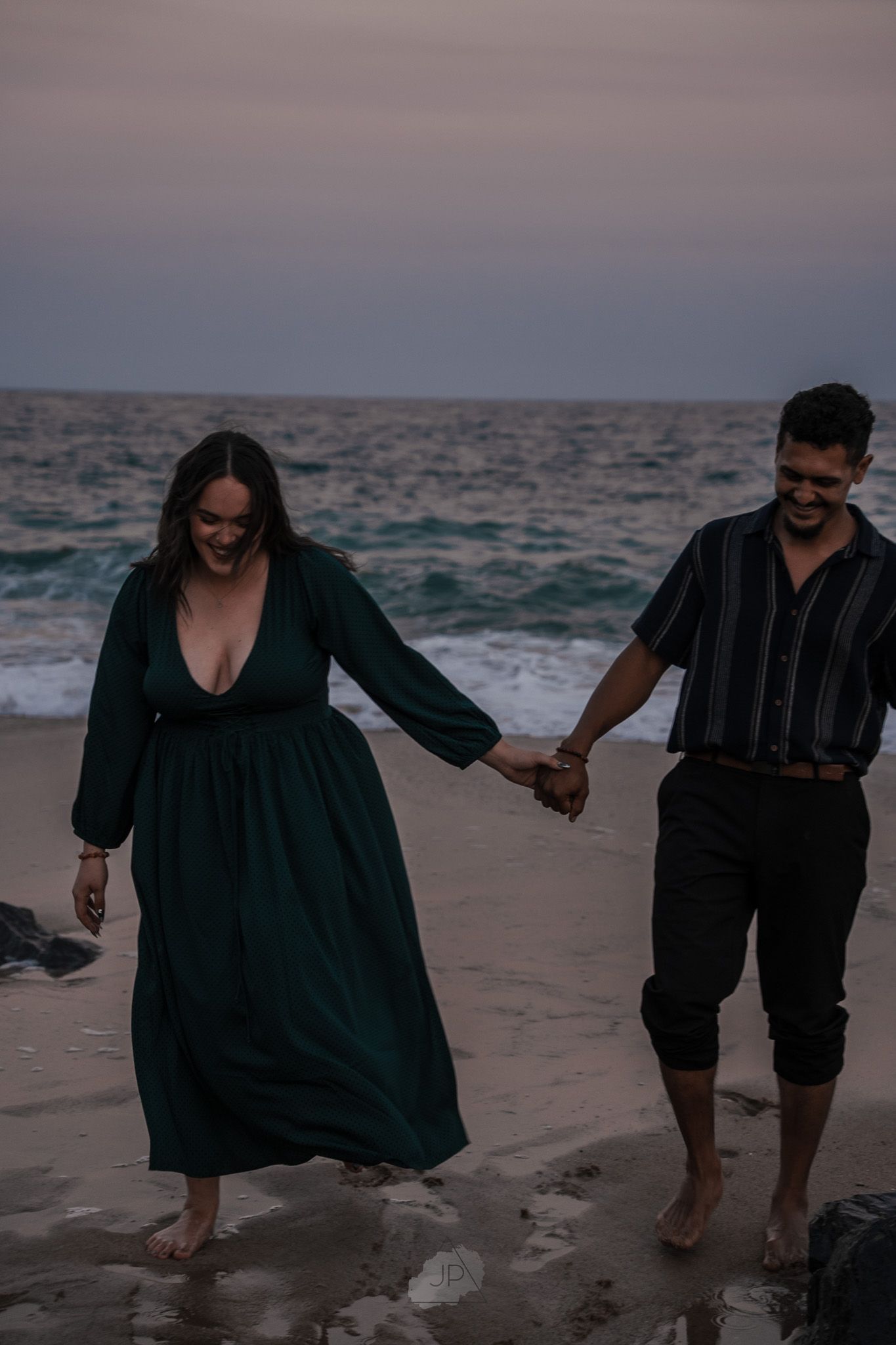 A couple walks hand in hand along a moody beach at dusk, creating a romantic silhouette against the ocean waves.