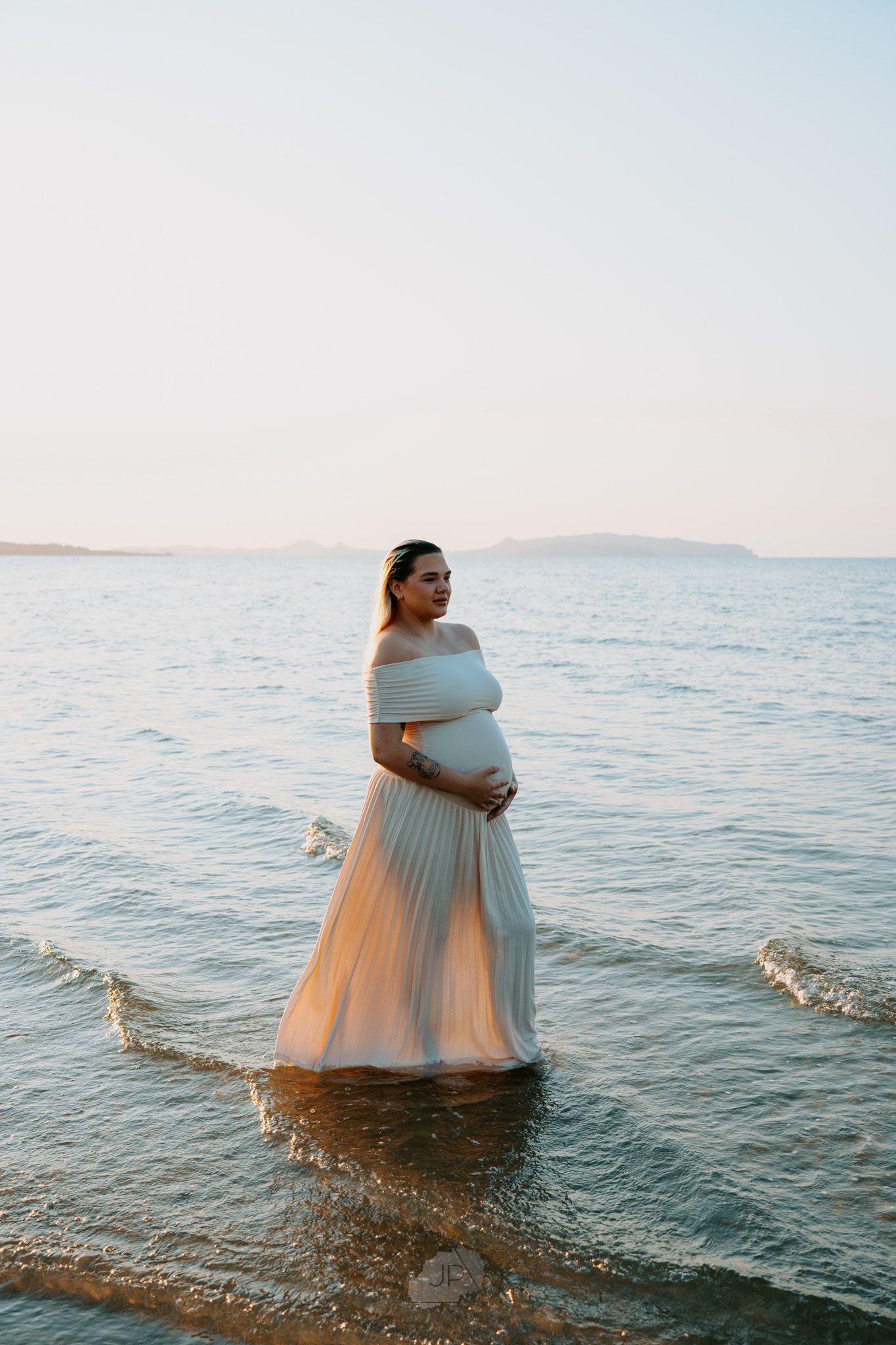 A person in a light blue dress stands in shallow ocean waters at sunset creating a dreamy coastal scene.
