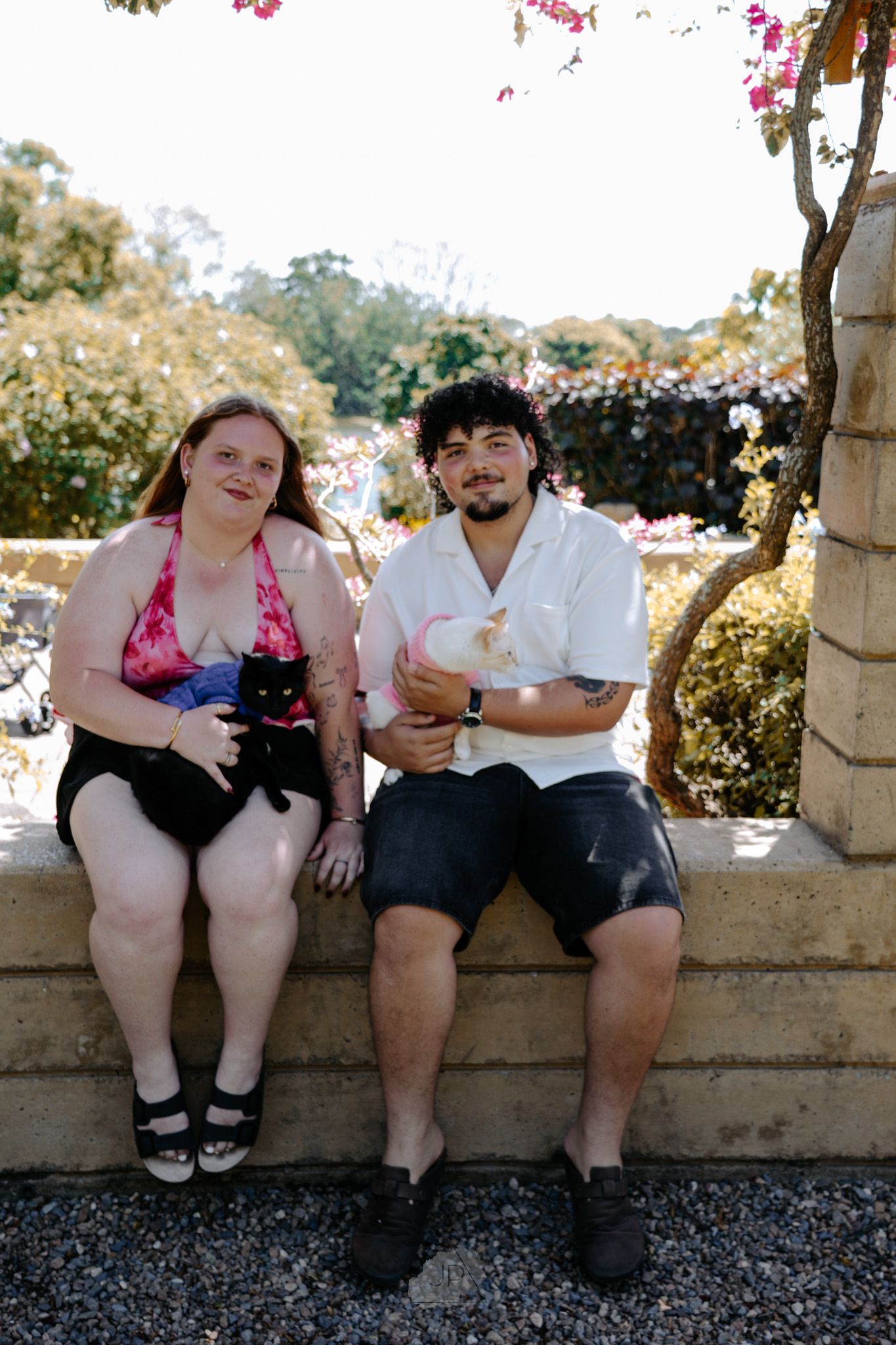 A couple sits together on a stone wall during a sunny outdoor photo session.