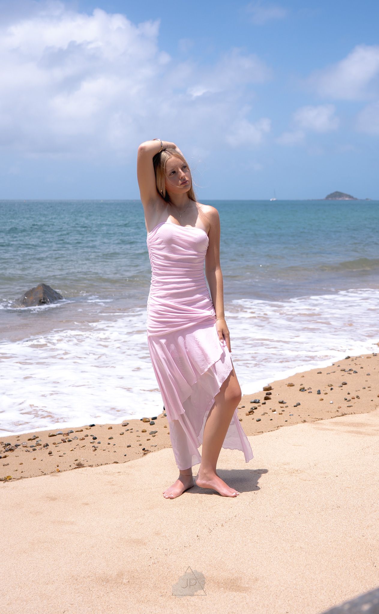 A person in a flowing pink dress poses gracefully on a tropical beach with turquoise waters and blue sky in the background.