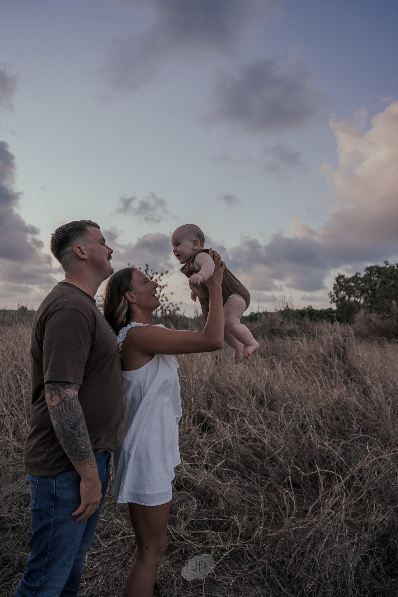 A tender family moment captured at sunset in a field of tall grass.