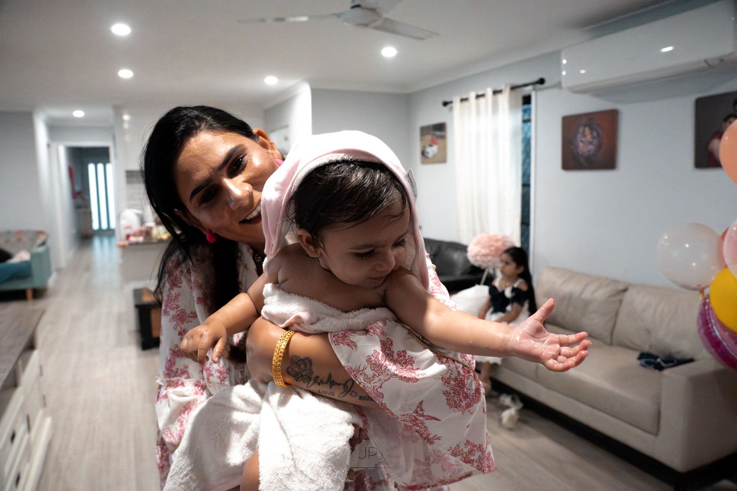 A caregiver and baby share a playful moment in a bright modern living room with gray furniture and white walls.