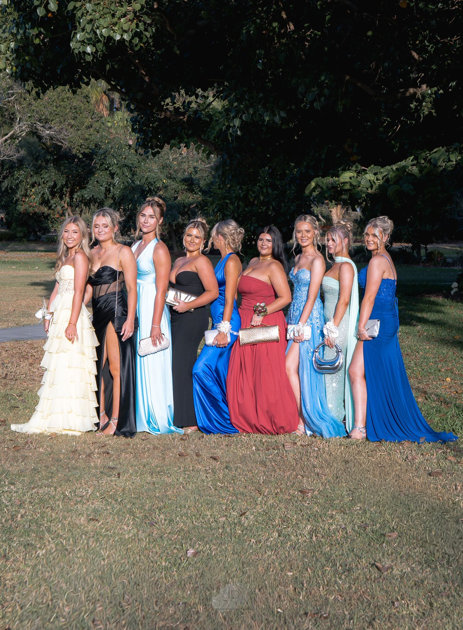 A group of women in blue and red dresses sit together on grass during an outdoor photo session.