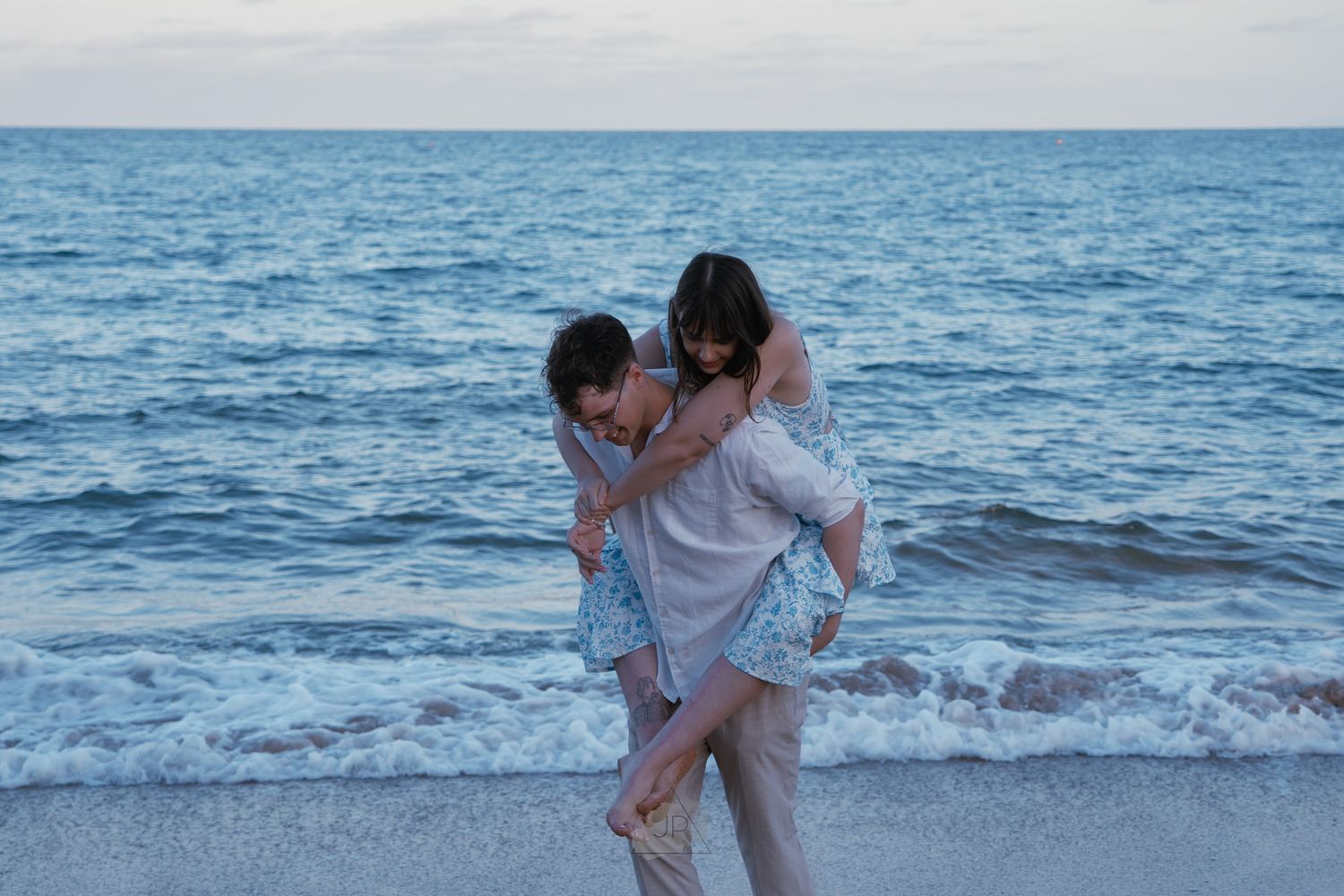 People enjoying a romantic moment together at the beach during sunset with waves crashing in the background.