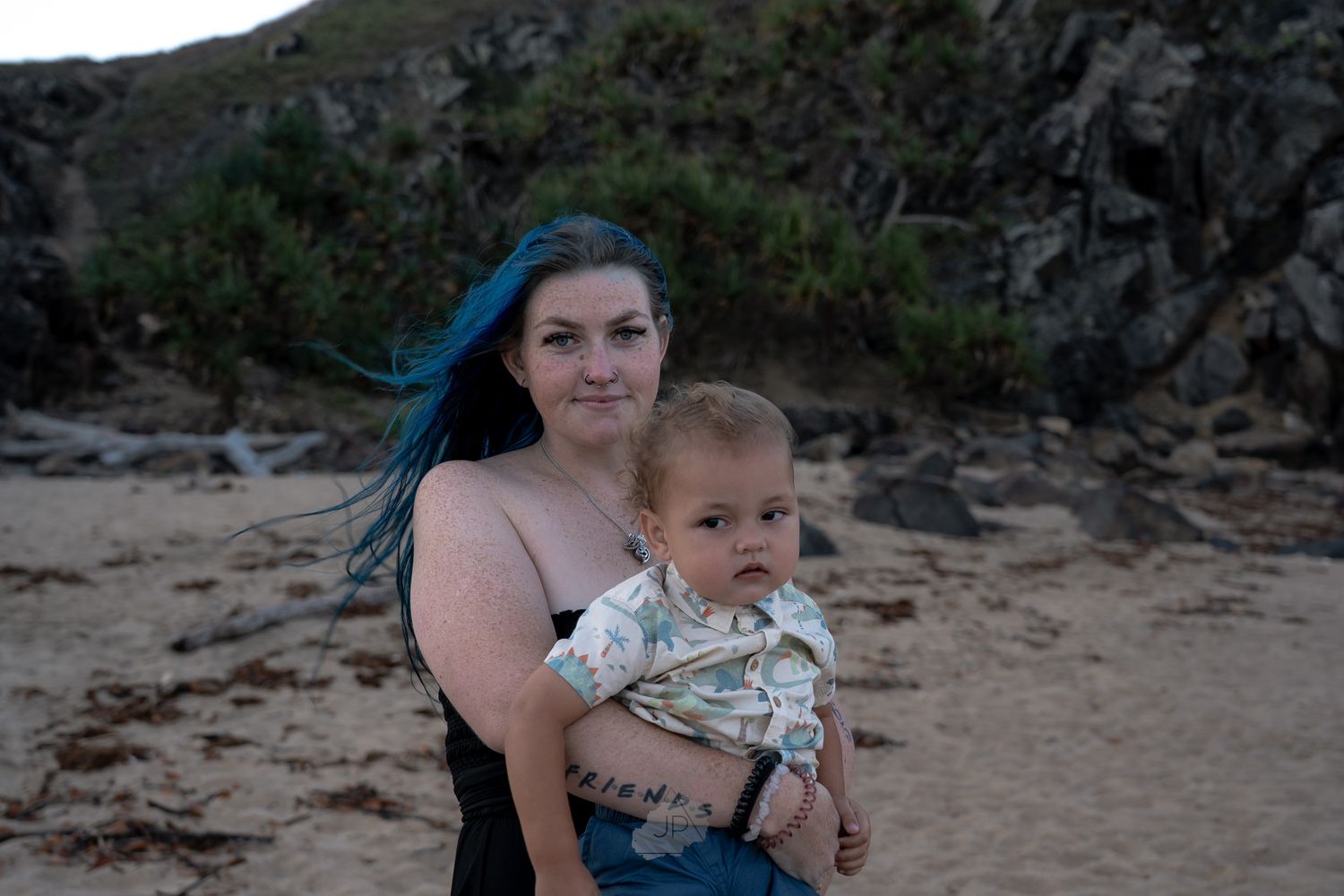 A person holds a small child while standing near a rocky beach area during sunset.