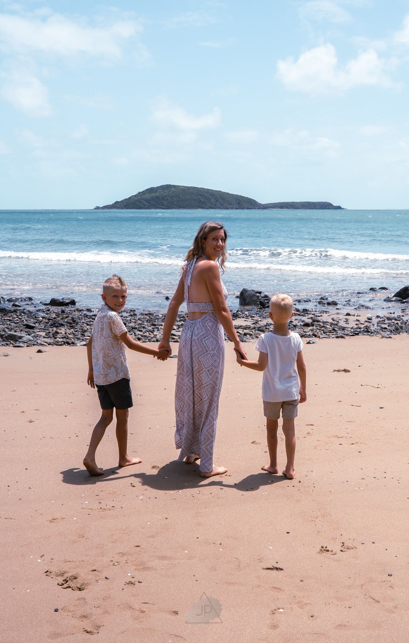 Family walking together on a tropical beach with an island visible in the distance on a sunny day.