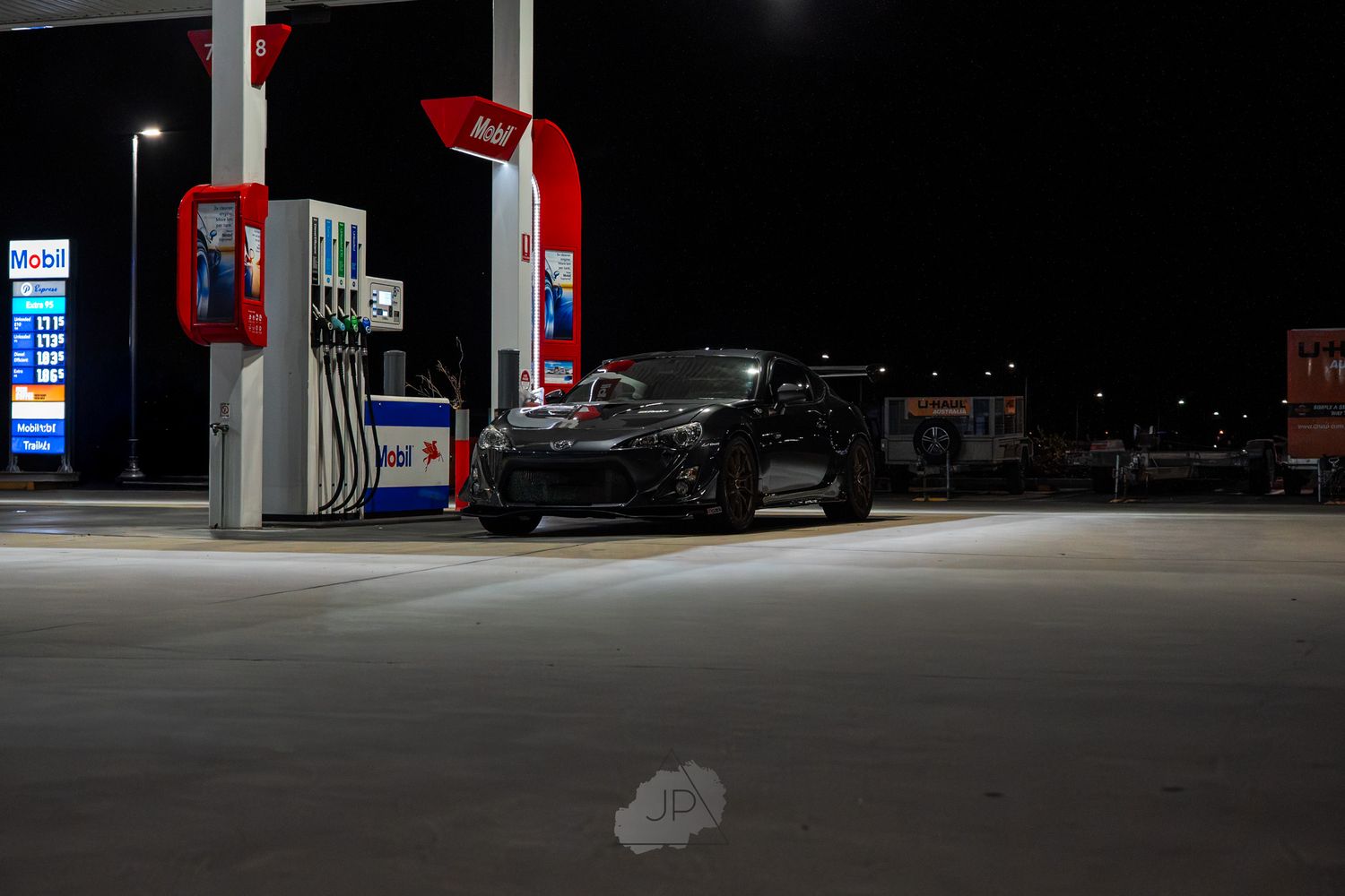 Illuminated gas station at night with black vehicle visible near fuel pumps.