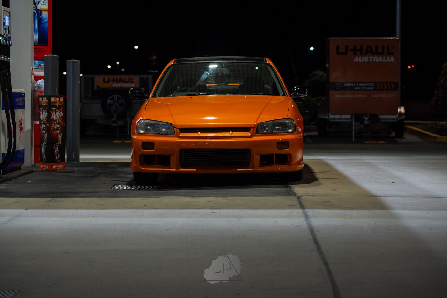 A series of five orange sports cars lined up in a dimly lit garage or showroom space.