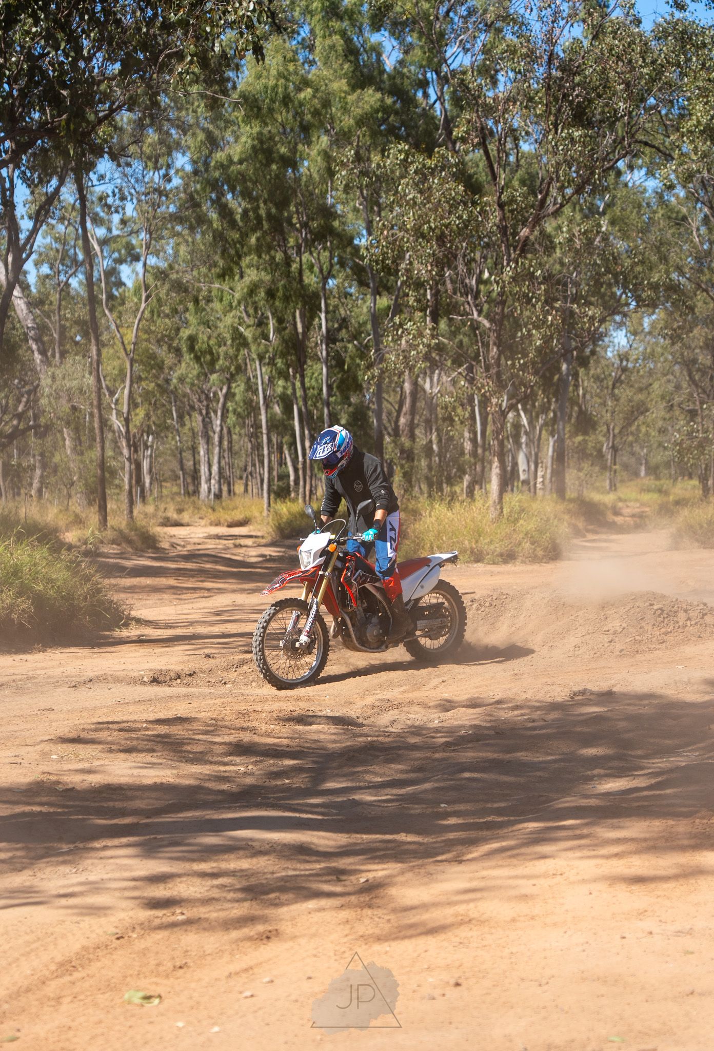 Multiple dirt bikes navigating a winding dirt track through an Australian bush setting with gum trees.
