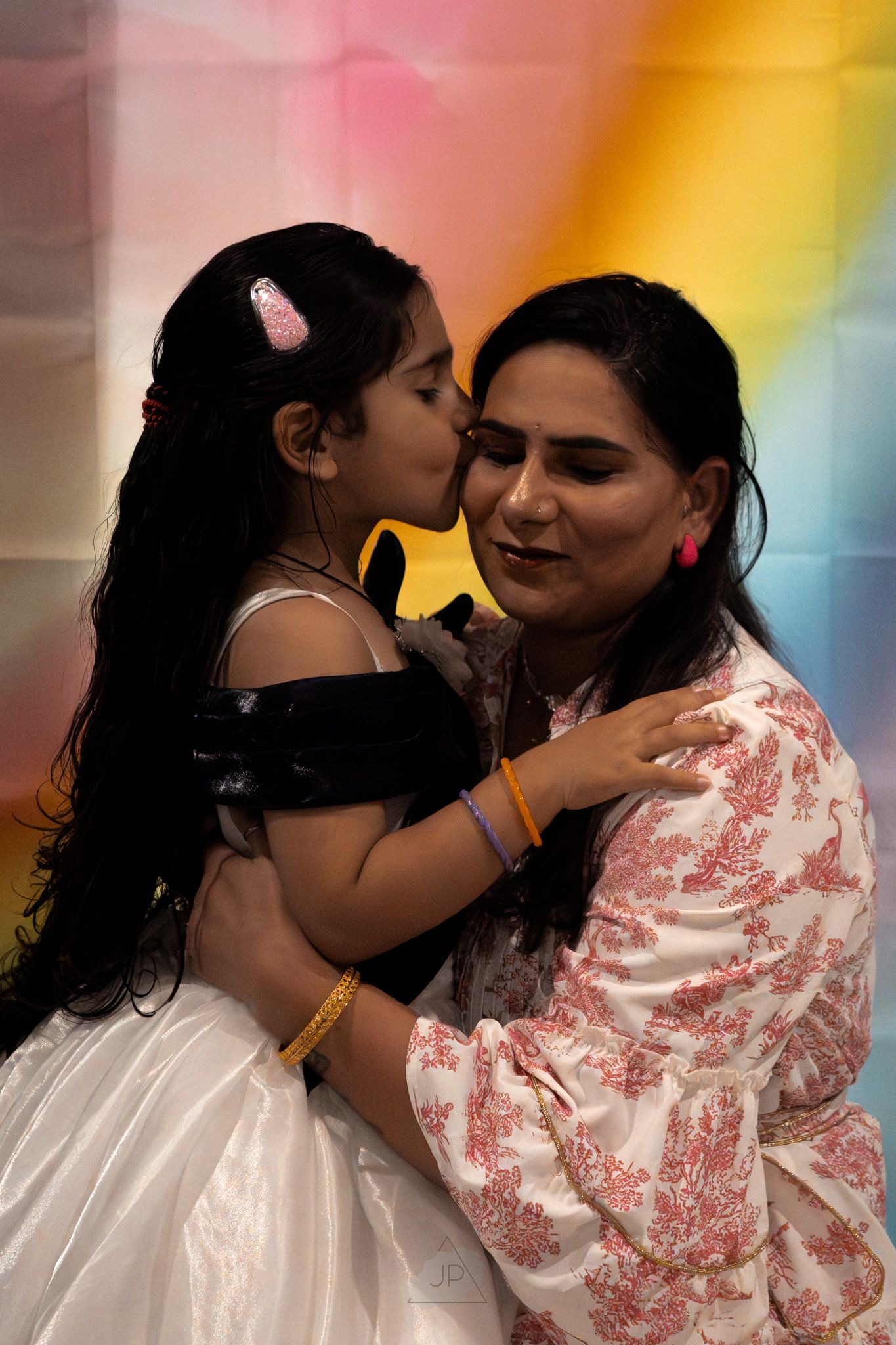Two people sharing an intimate moment against a colorful rainbow background with soft lighting effects.