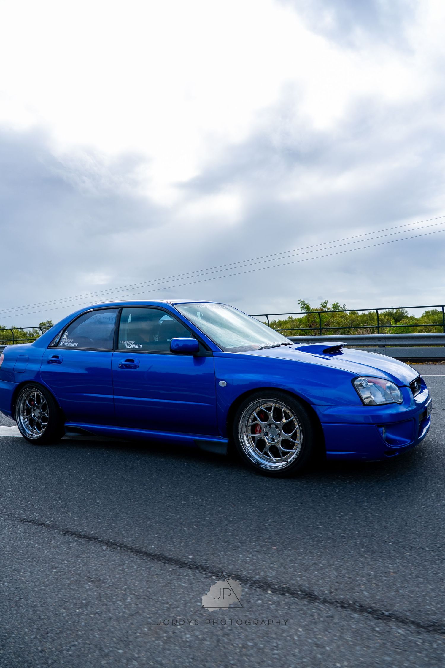 Modified blue Subaru WRX with custom wheels and lowered suspension shown from multiple angles on asphalt.