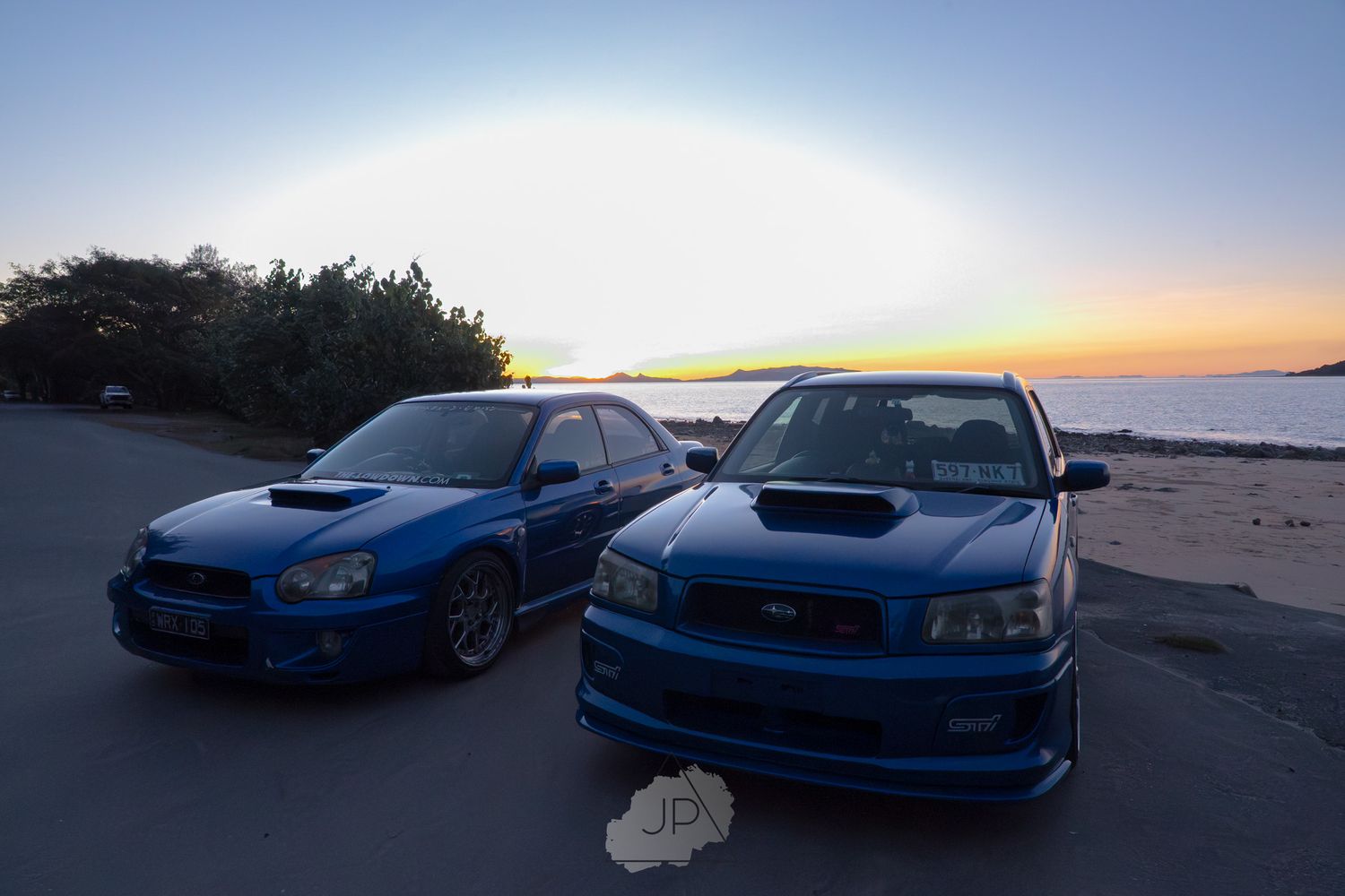 Line of blue Subaru WRX sports cars parked along coastal road during sunset.