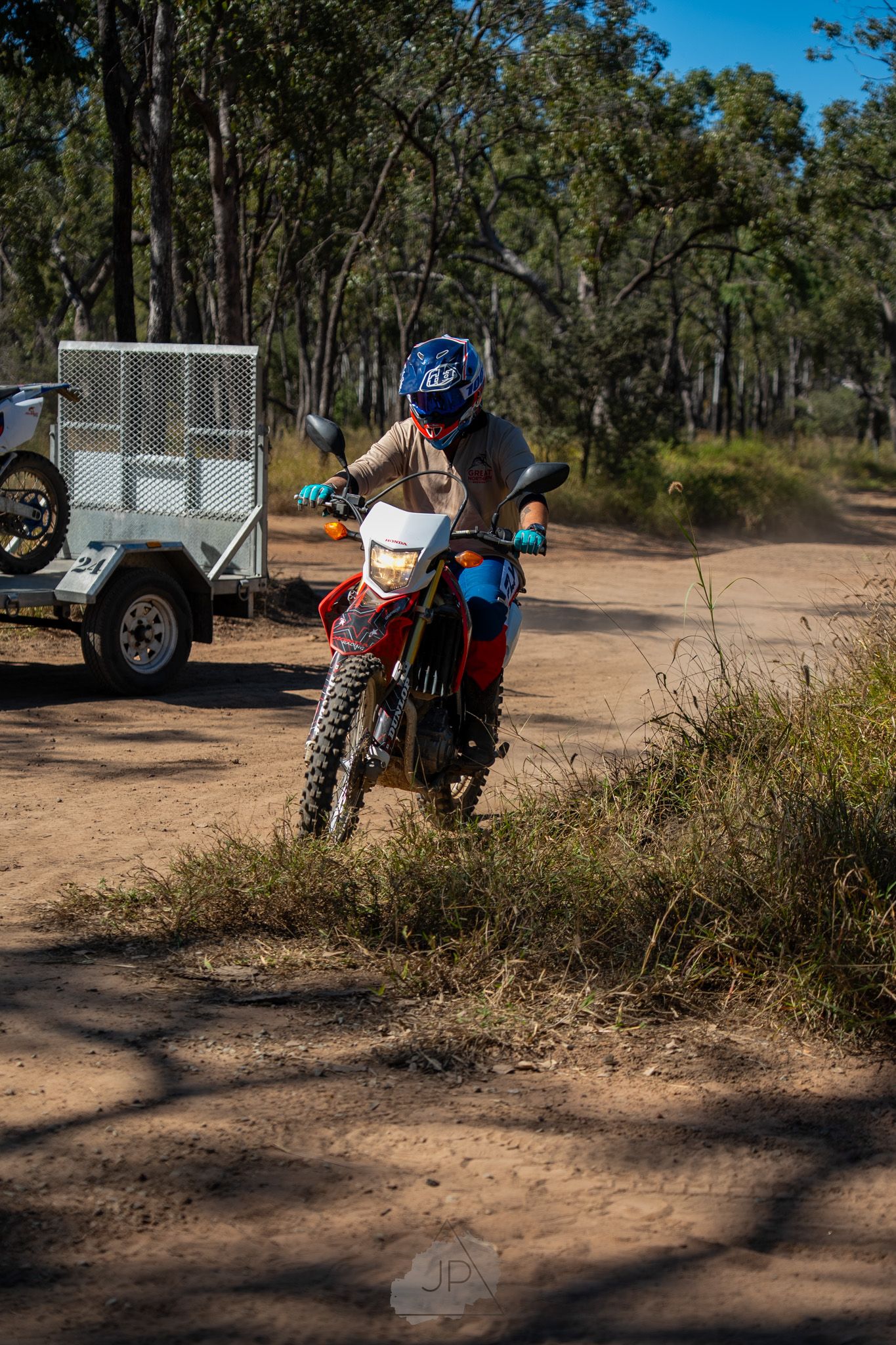 Motorcycle and trailer parked on dusty outback trail surrounded by eucalyptus trees in Australian bush setting.