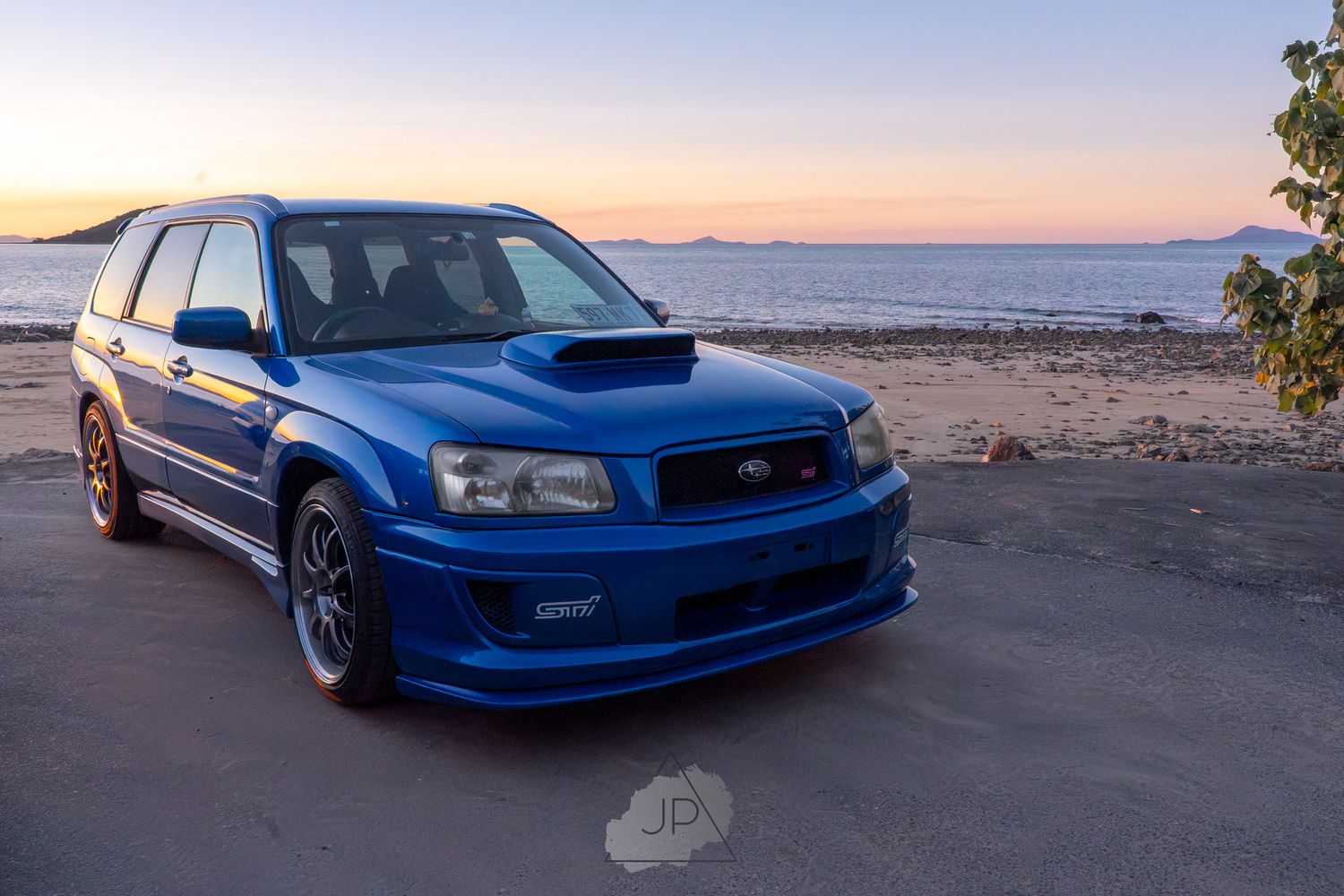 A bright blue Subaru Legacy sports car photographed at sunset by the ocean in multiple angles.