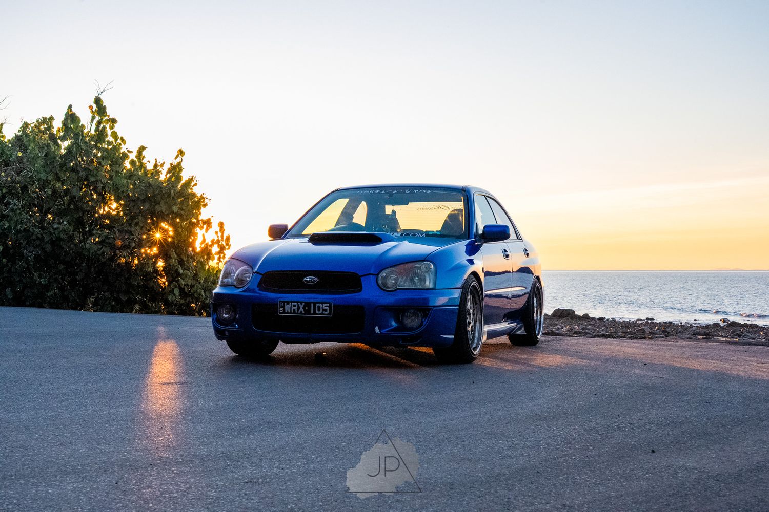 A bright blue sports car parked at a scenic seaside location during a golden sunset.
