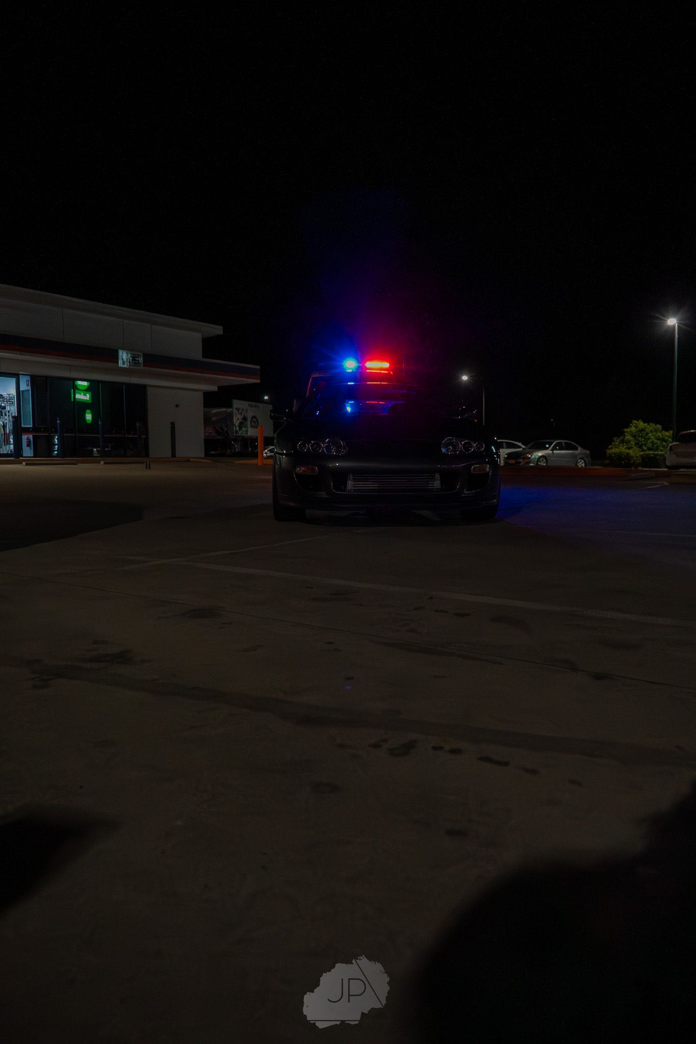 Police vehicle with flashing red and blue emergency lights illuminating a dark parking lot at night.