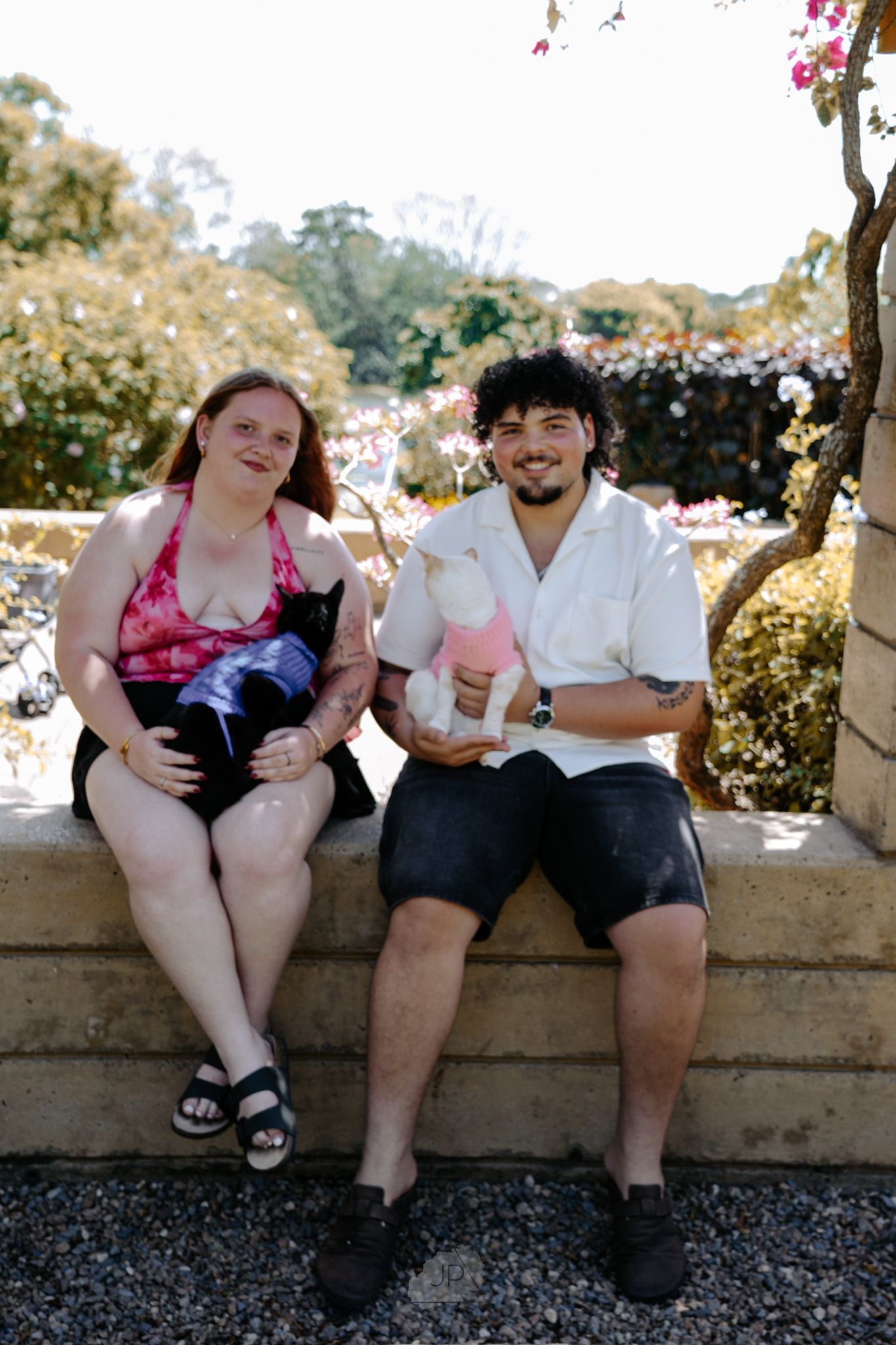 Two people sit on a stone wall wearing summer clothes while enjoying ice cream cones together.