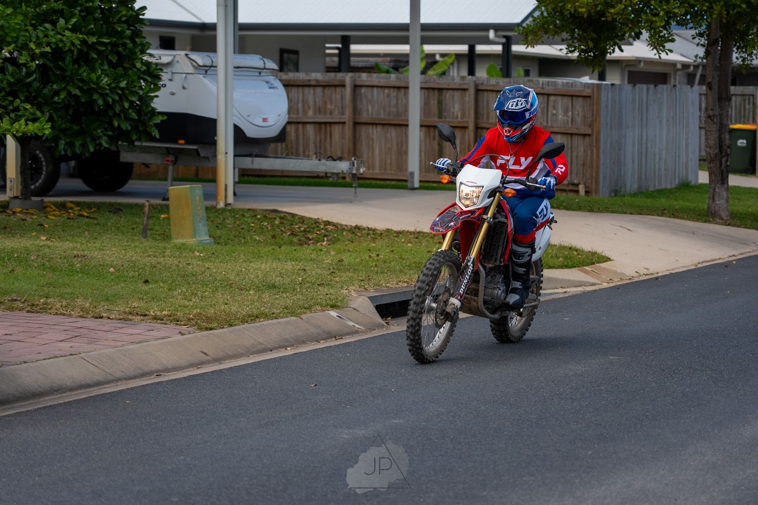 A red and blue motorcycle parked at the beginning of a winding suburban street.
