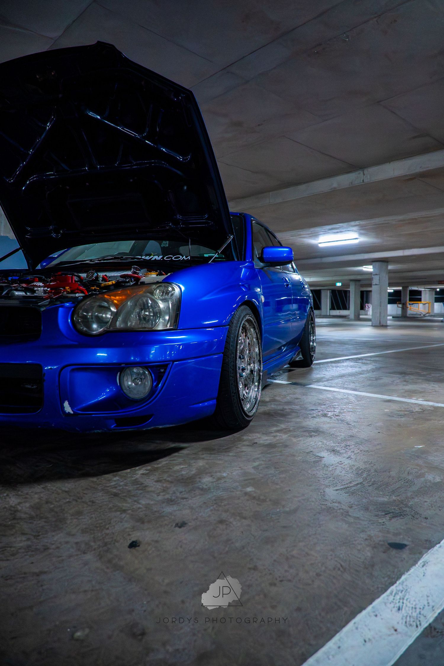Blue modified Honda Civic shown from different angles in a dimly lit parking garage with exposed hood and aftermarket wheels.