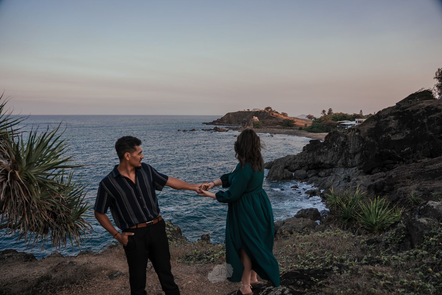 A couple enjoys a scenic sunset view while sitting on rocky coastal cliffs overlooking the ocean.