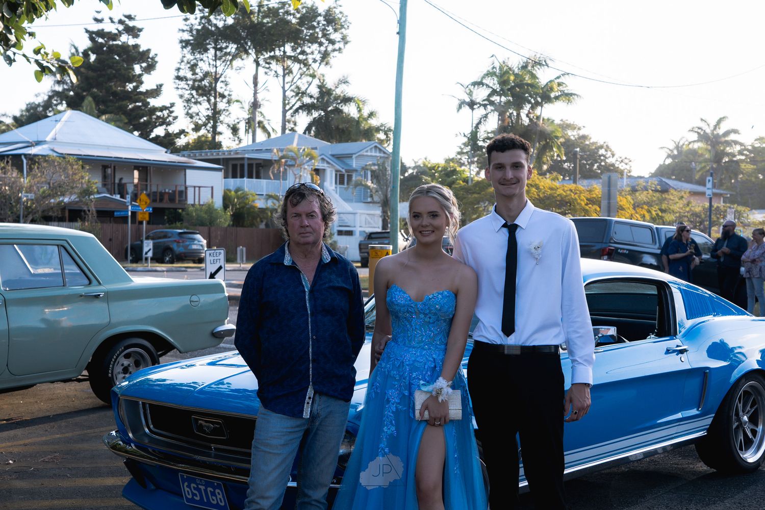 A group stands beside a classic blue and white vintage car at an outdoor event during sunset.