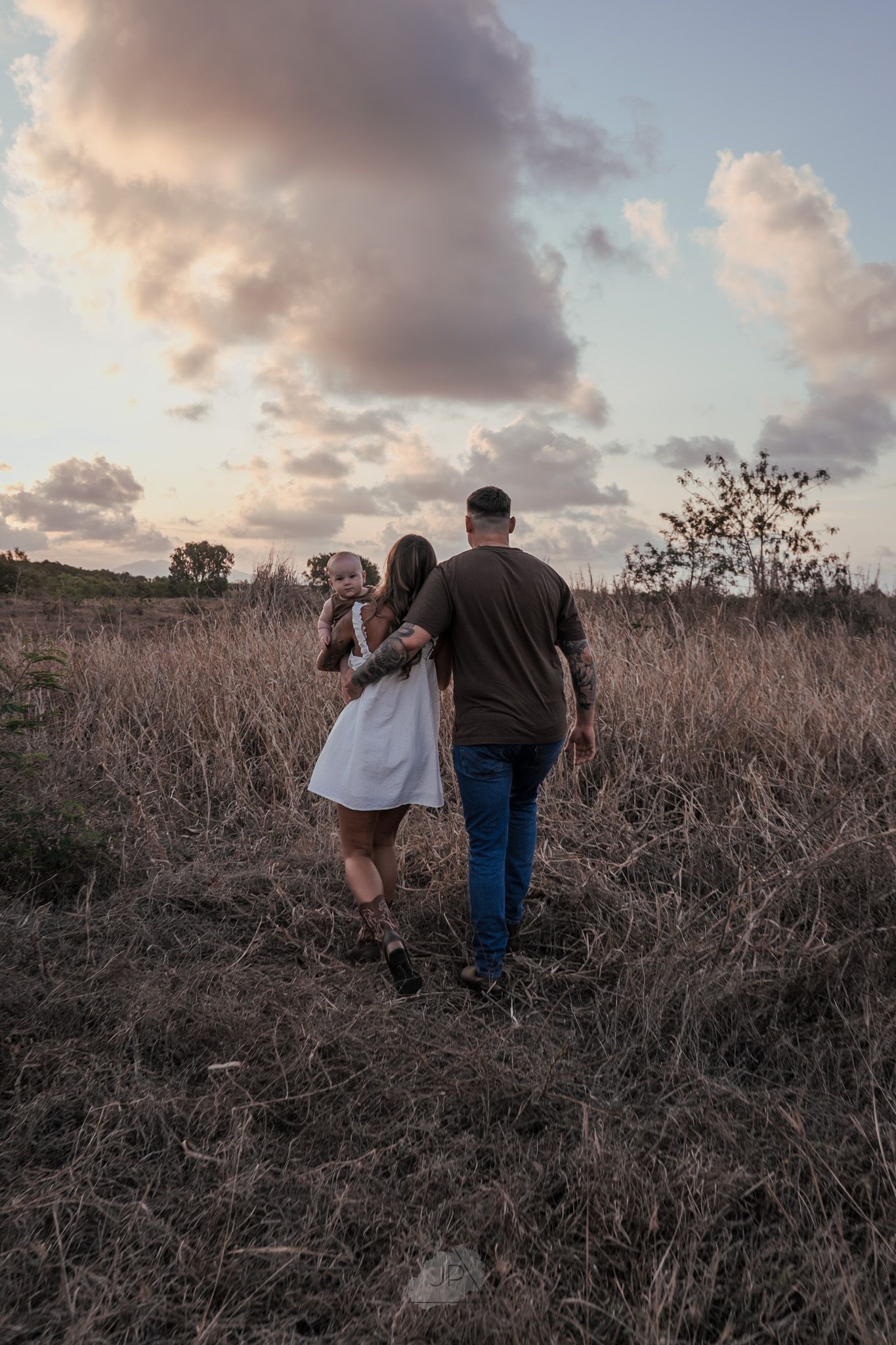 Two people walk through a field of dried brush during sunset with dramatic clouds in the sky.