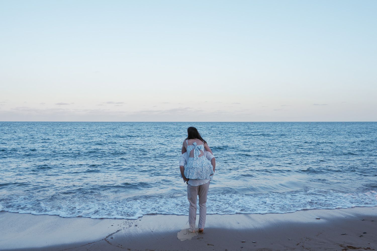 Panoramic view of a serene beach with gentle waves rolling onto the sandy shore under a soft blue sky.