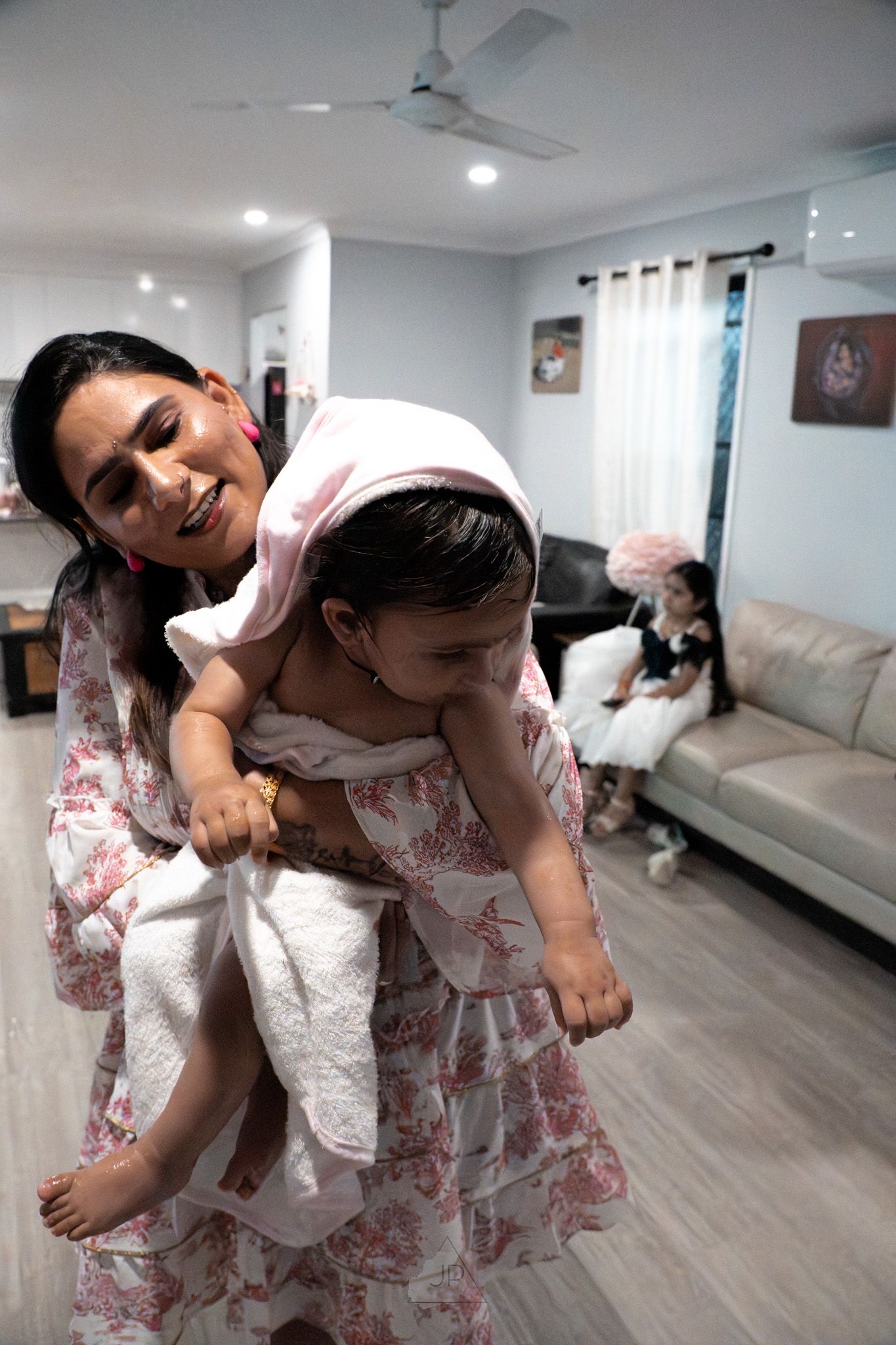 A parent and child in matching floral outfits share playful moments on a light wood floor with white furniture.