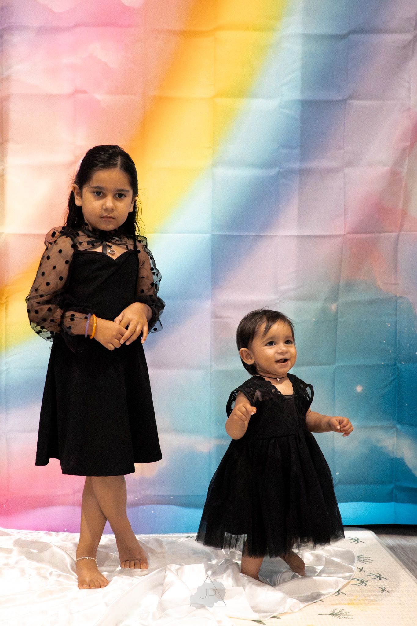 A sequence of five photos showing a small child in a black dress posing playfully against a rainbow-colored backdrop.