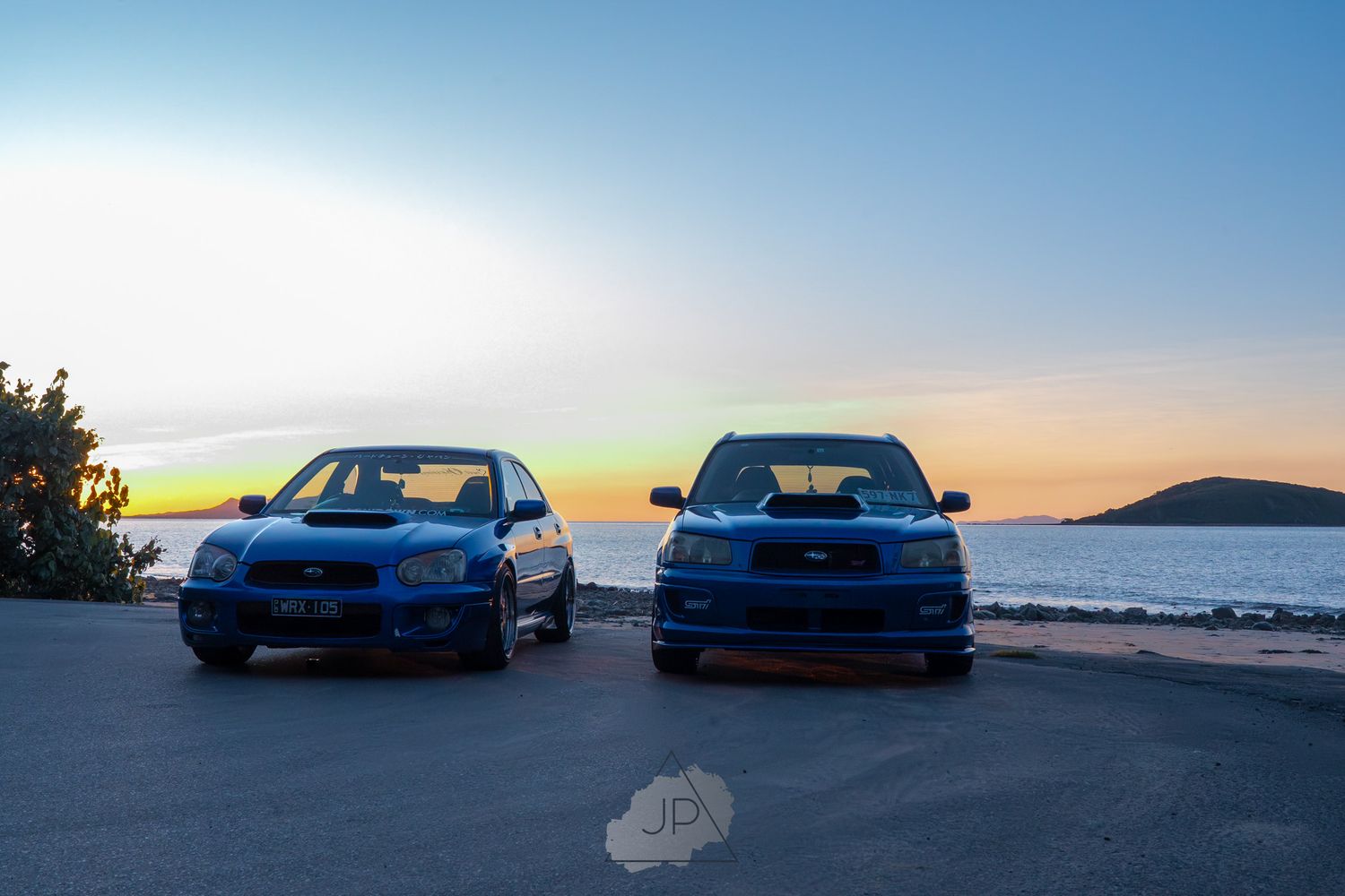 A sleek blue WRX STI sports car parked with lake and mountain views during sunset creates a stunning automotive scene.