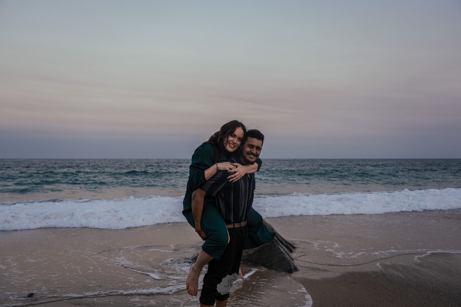 People enjoying a romantic sunset walk along a scenic beach shoreline with waves crashing in the background.