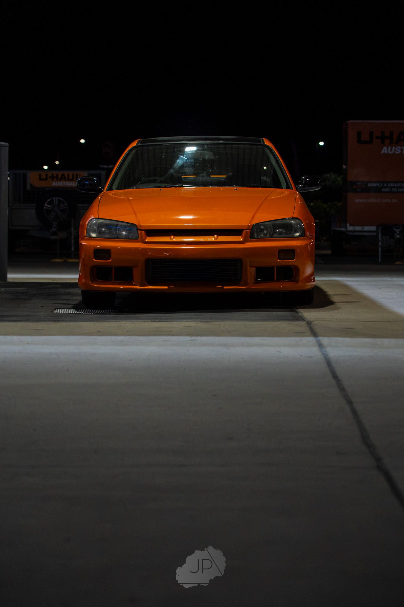 Orange Honda Civic sports car parked at night in an empty parking lot with dramatic lighting.