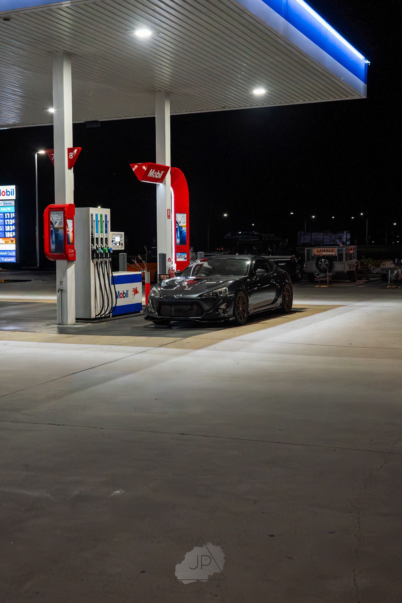 Nighttime view of a modern gas station with bright LED lighting illuminating the fuel pumps and concrete forecourt.