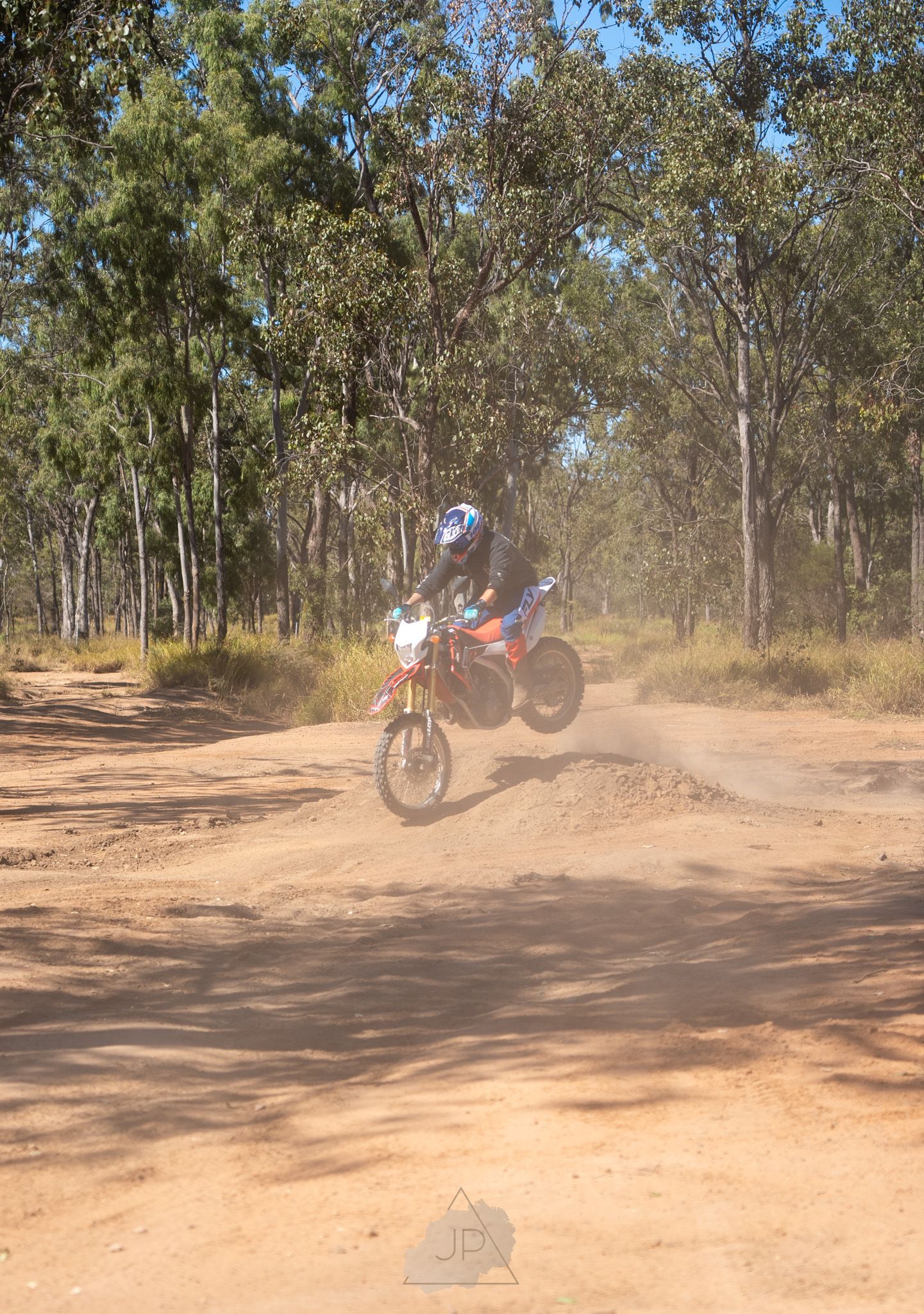 Dirt bike rider performing a high-speed turn on a dusty off-road trail through eucalyptus trees in Australia.