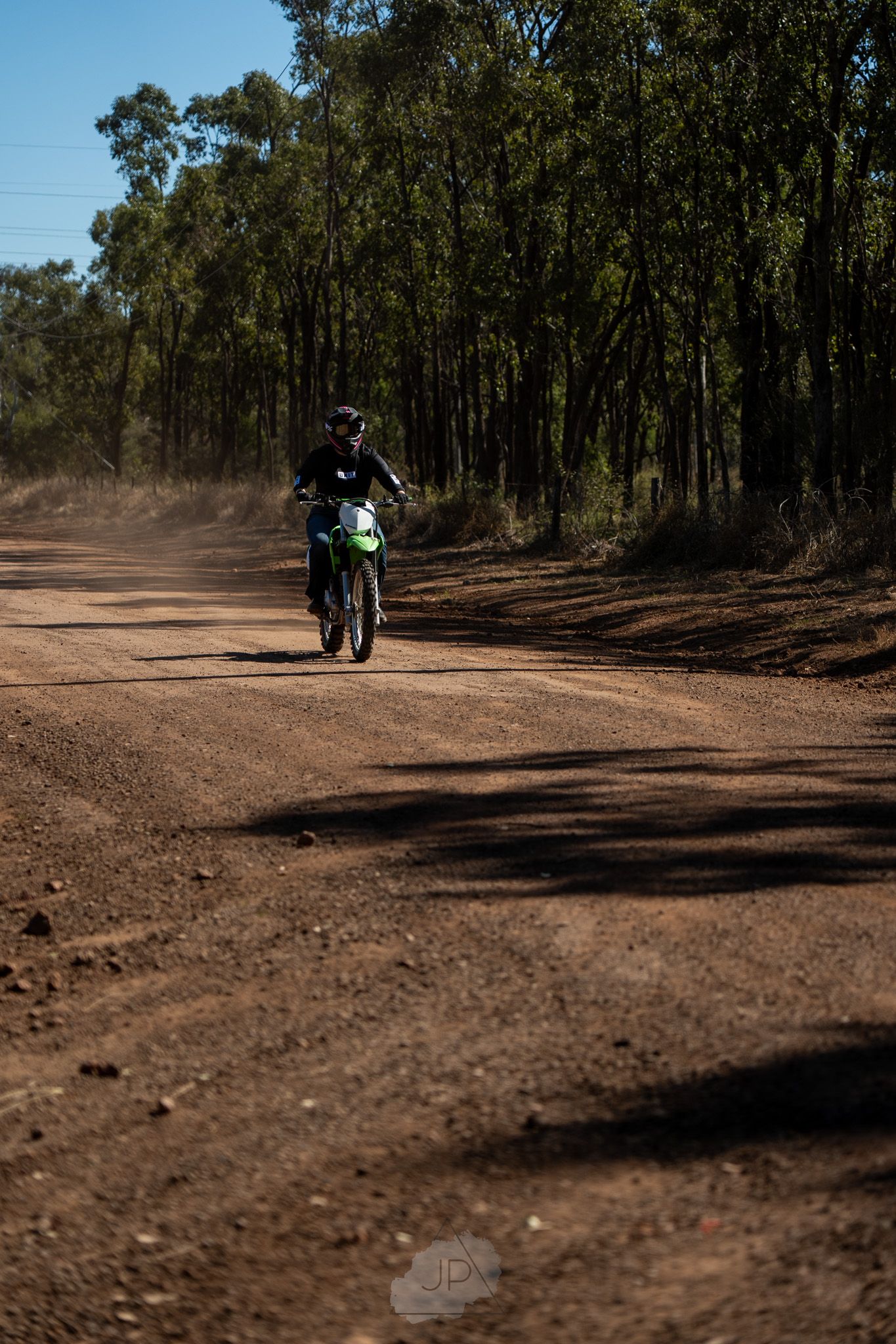 A dirt trail winding through a eucalyptus forest with bike riders in the distance on a sunny day.